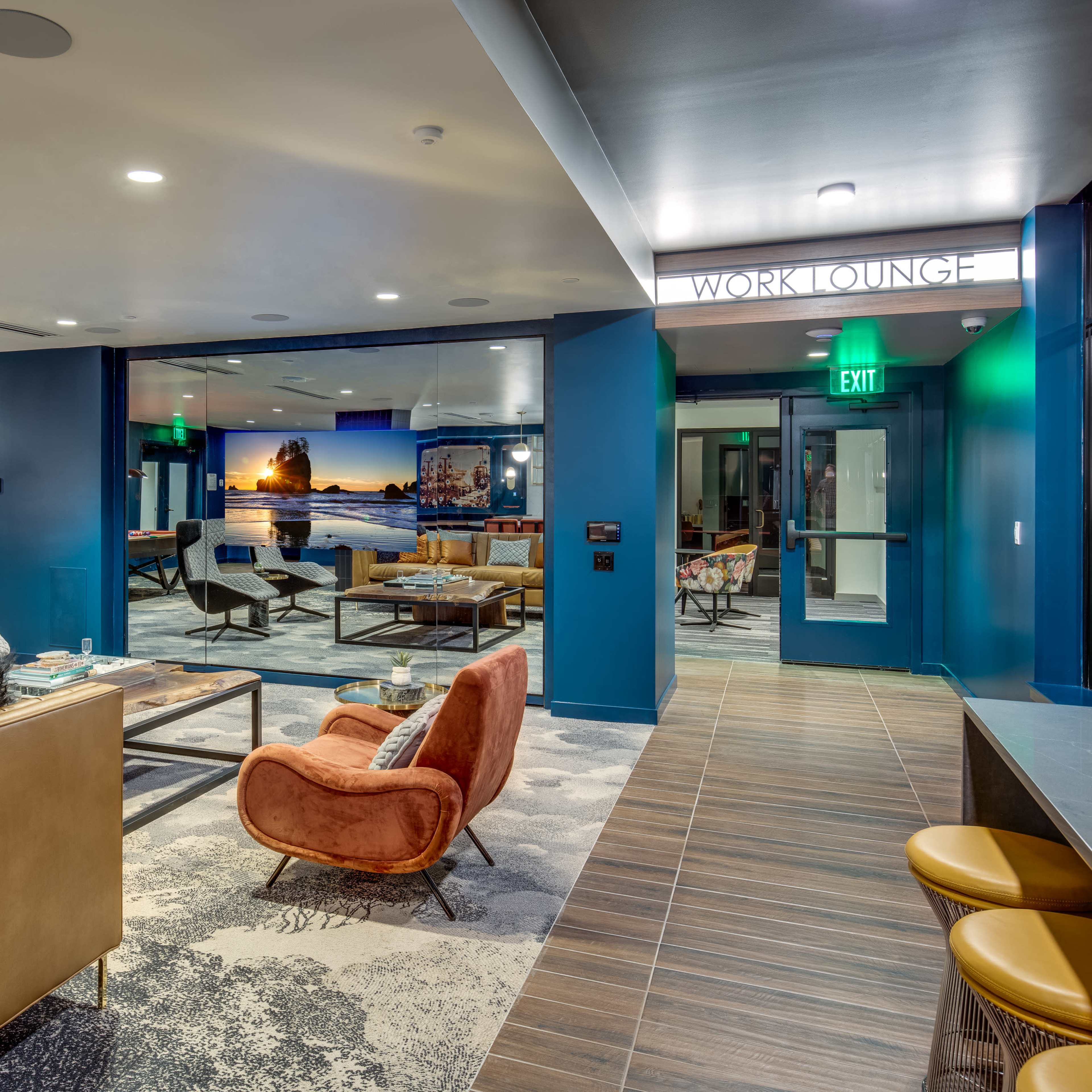 A modern work lounge featuring cozy seating, workstations, and blue walls, designed for collaboration and relaxation.