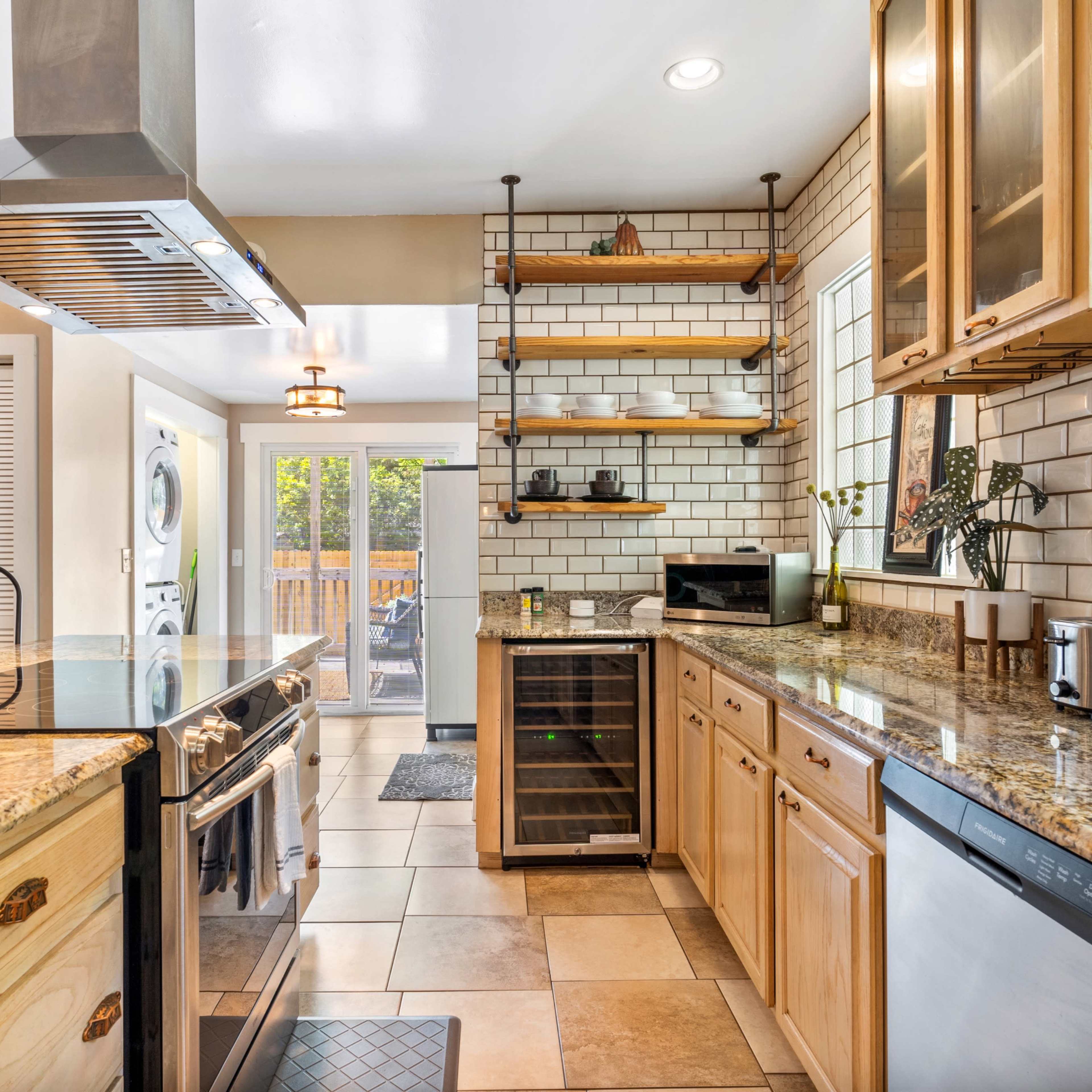 A modern kitchen with wooden cabinets, granite countertops, and stainless steel appliances, featuring an open layout with a view into an outdoor space.