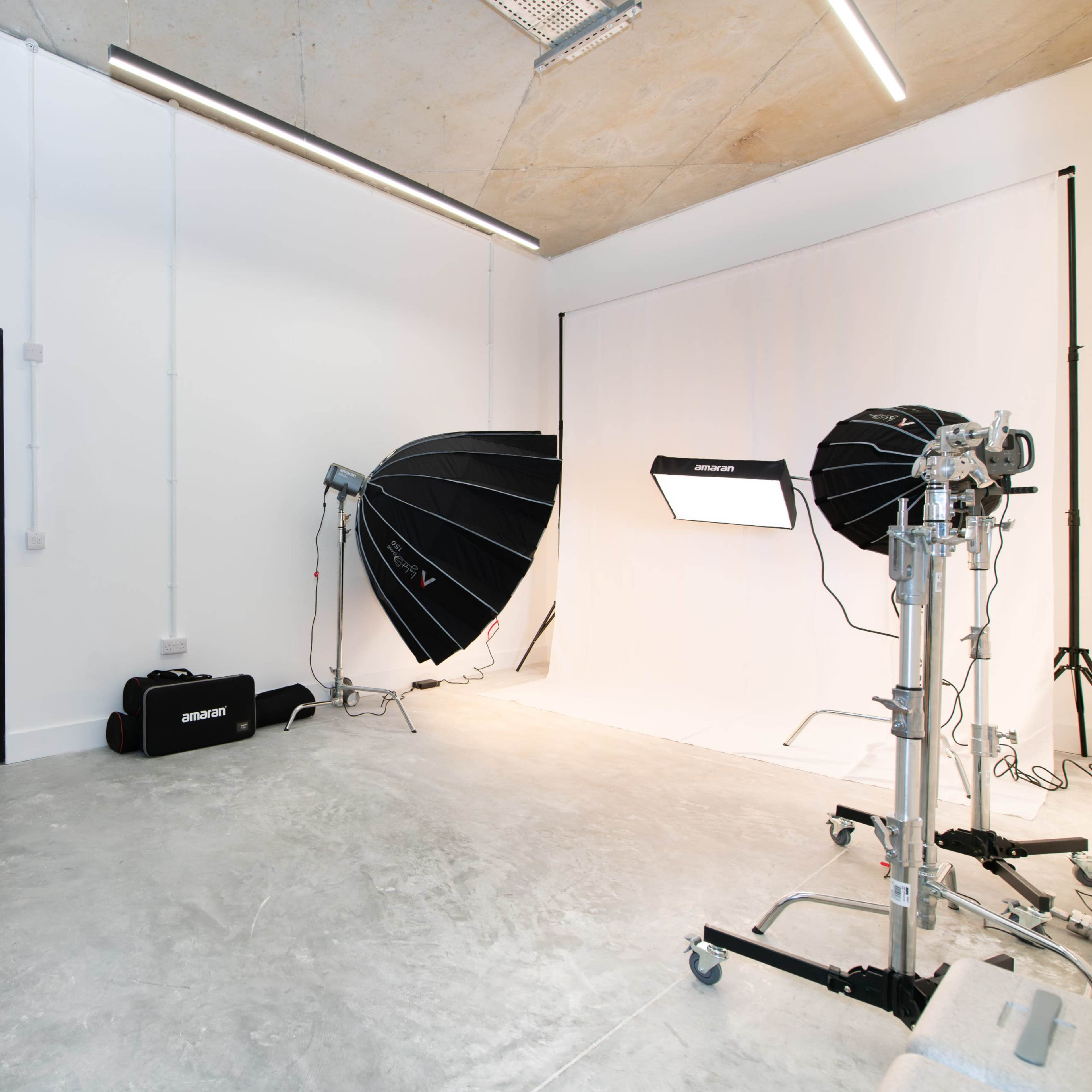 A photography studio with two large softbox lights, a plain white backdrop, and colorful stools arranged in front of the setup.