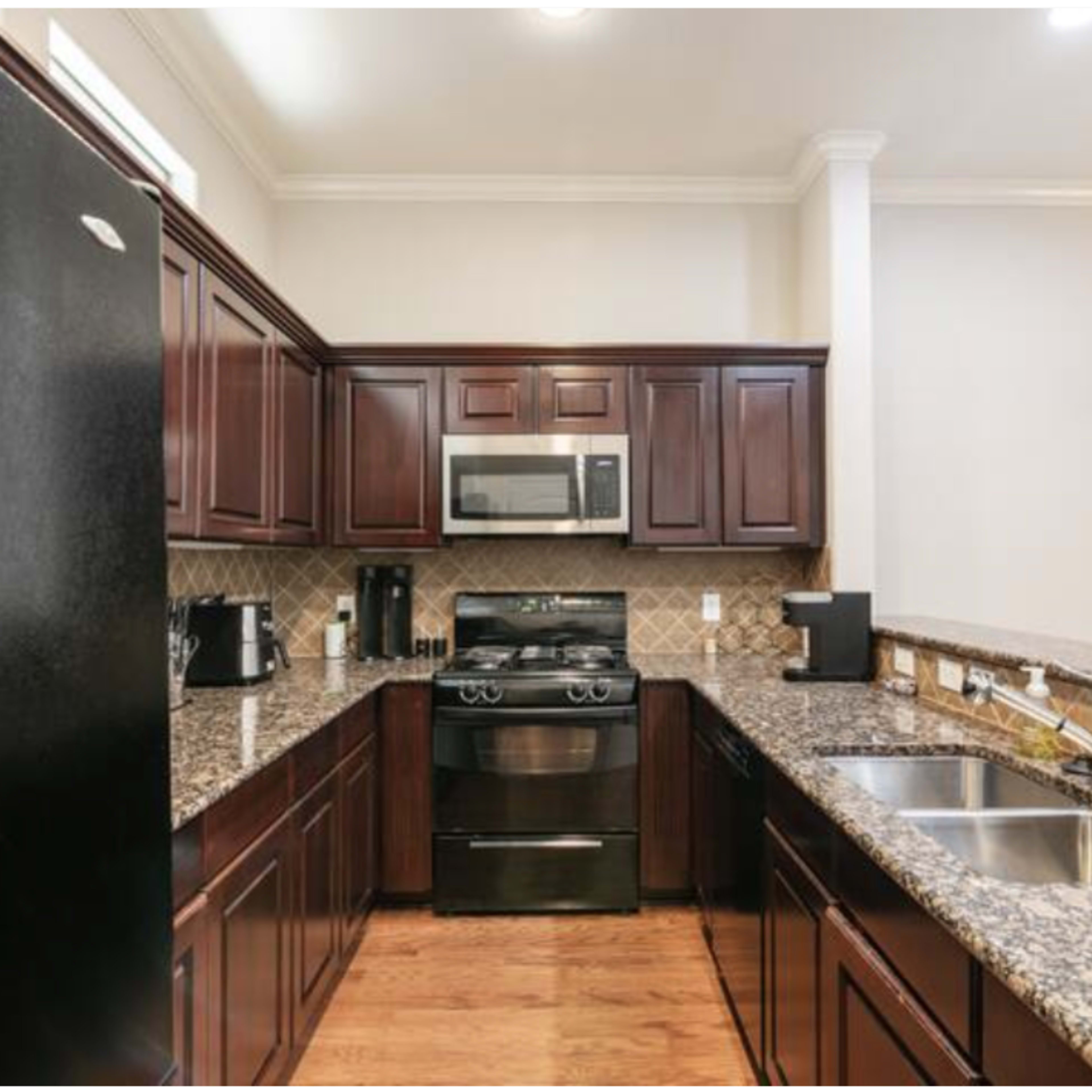 A modern kitchen with dark wooden cabinets, granite countertops, a stainless steel refrigerator, and a double sink.