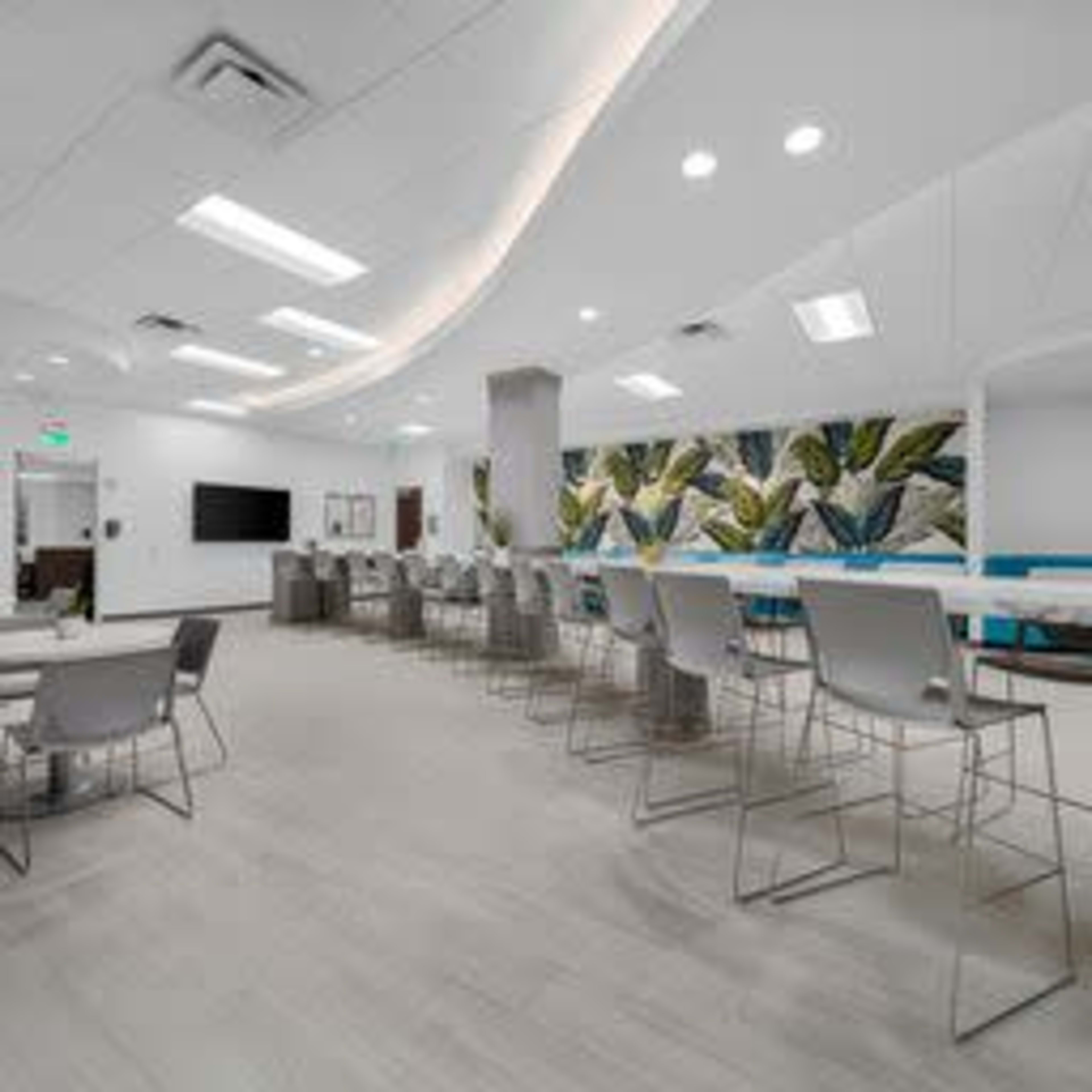 A modern, open office space with light-colored flooring, multiple seating areas, and a large mural of foliage on one wall.
