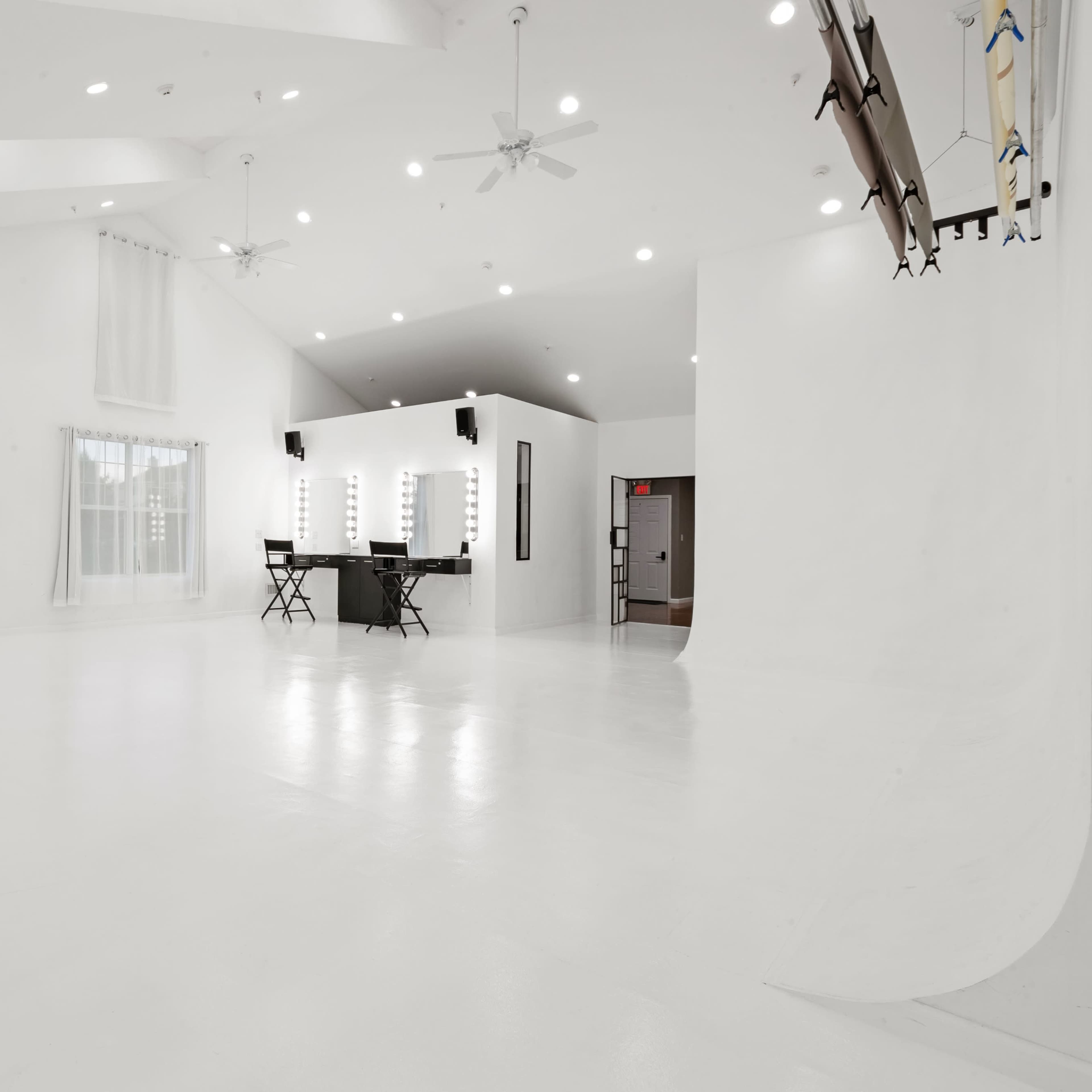 A spacious, bright white studio with large windows, a mirrored wall, and a makeup station with lights.