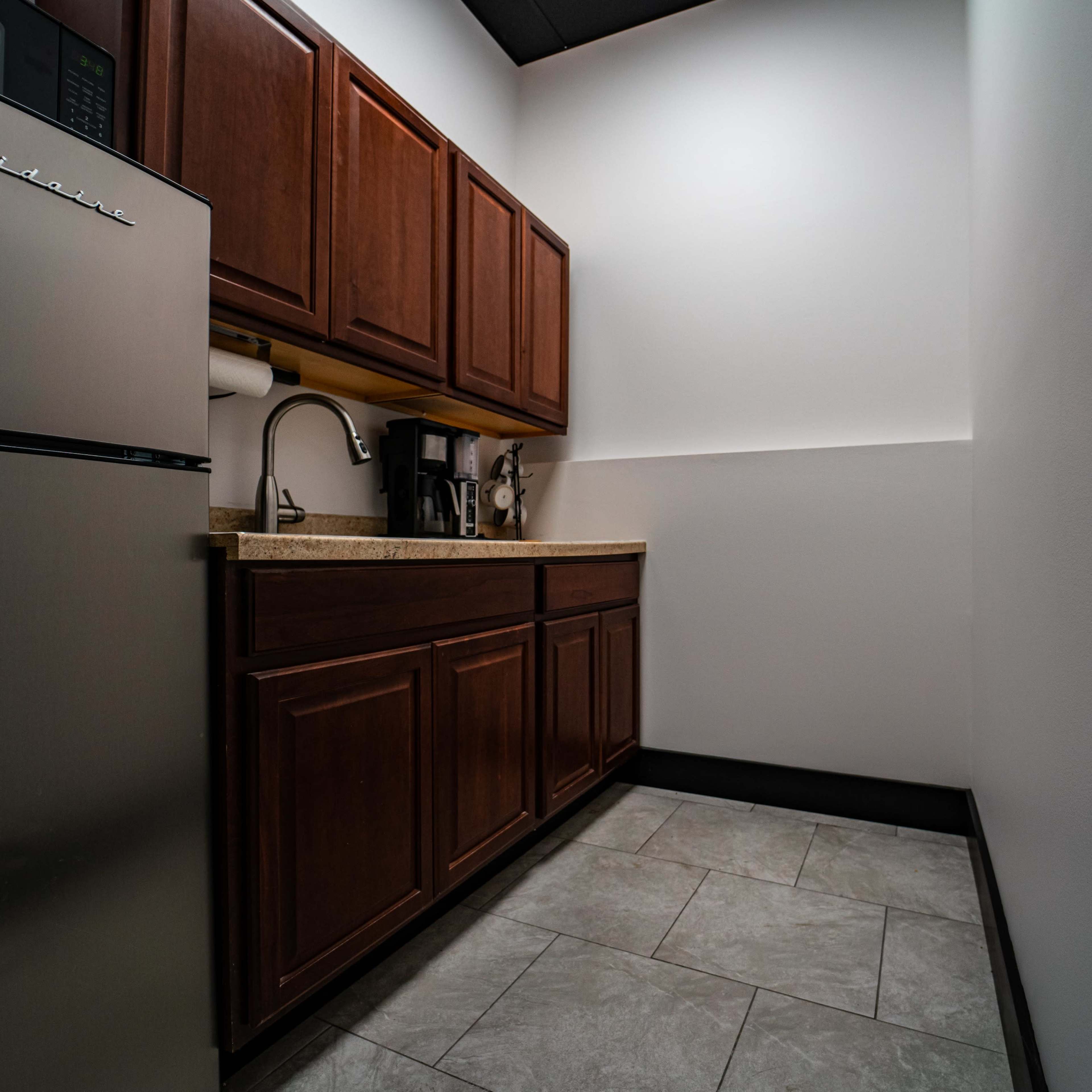 A small kitchenette features dark wooden cabinets, a stainless steel refrigerator, and a countertop with a coffee maker and sink.