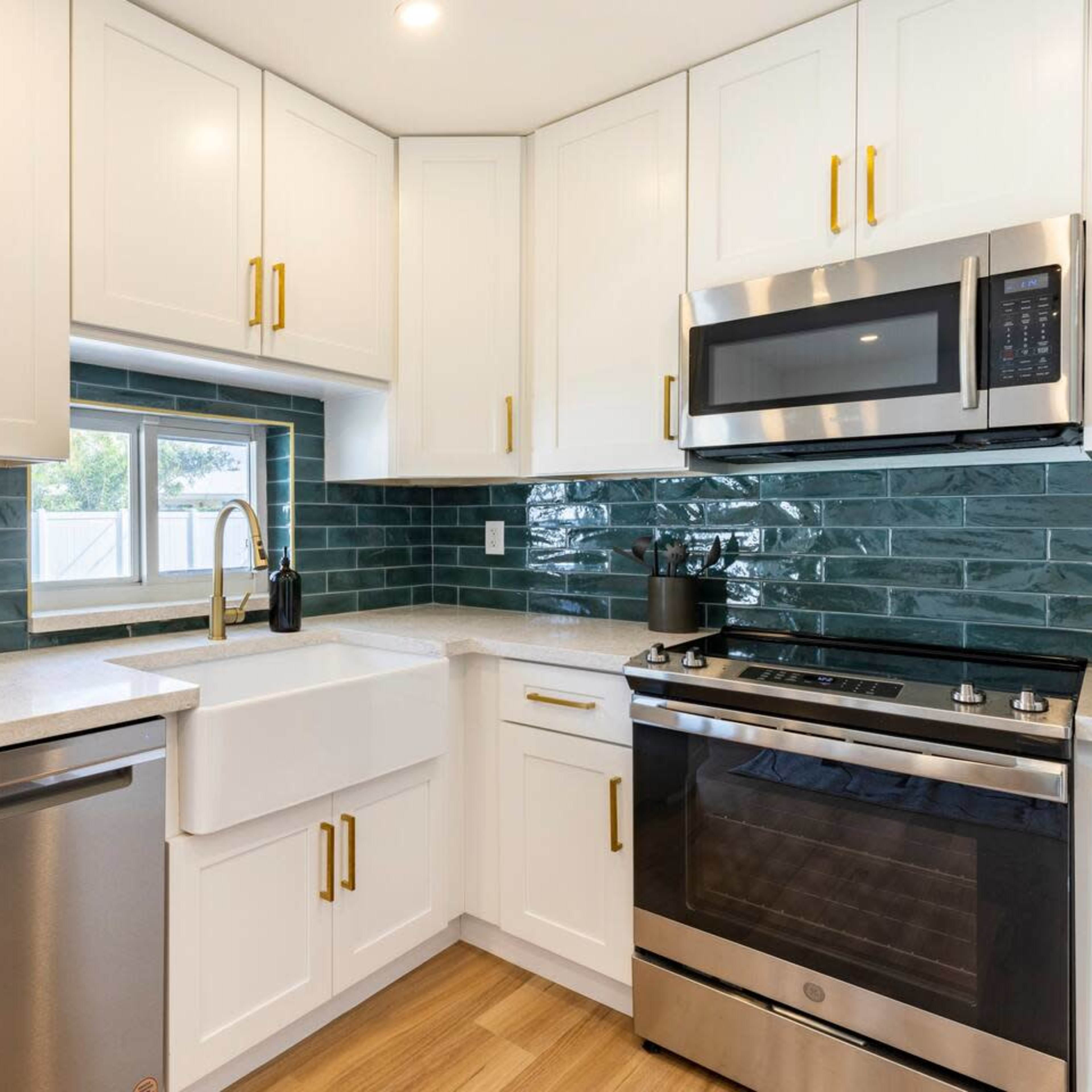 A kitchen with white cabinets, a farmhouse sink, stainless steel appliances, and teal subway tile backsplash.