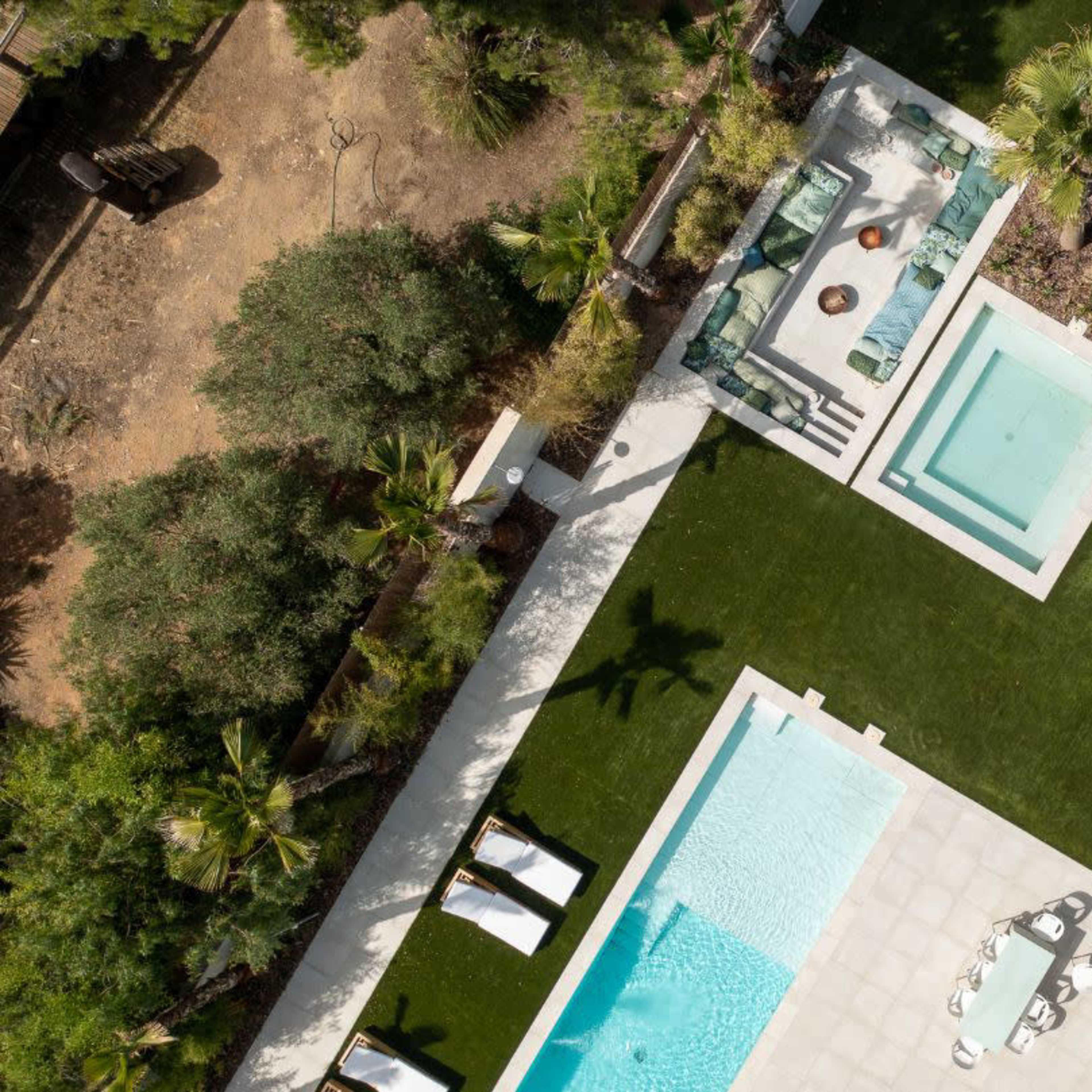 An aerial view of a modern outdoor space featuring a swimming pool, spa, lounge areas, and landscaped greenery.