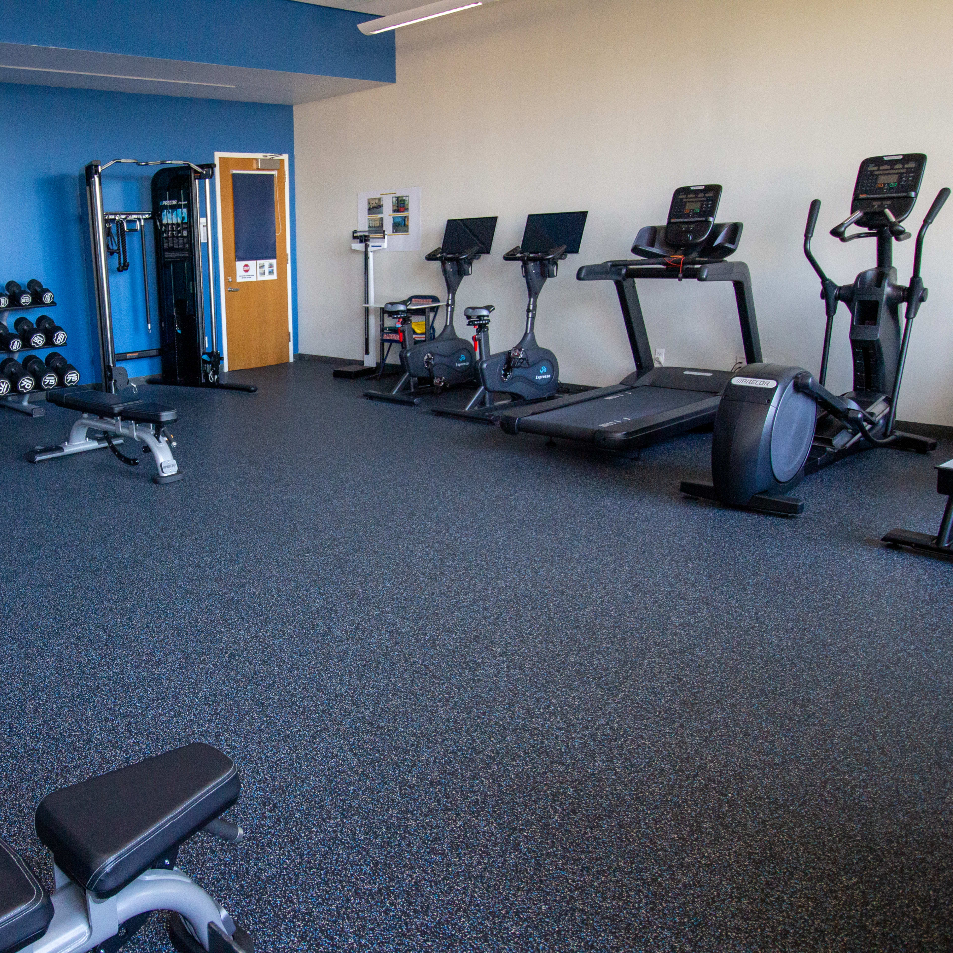 A fitness room equipped with various exercise machines, free weights, and a stretching area.