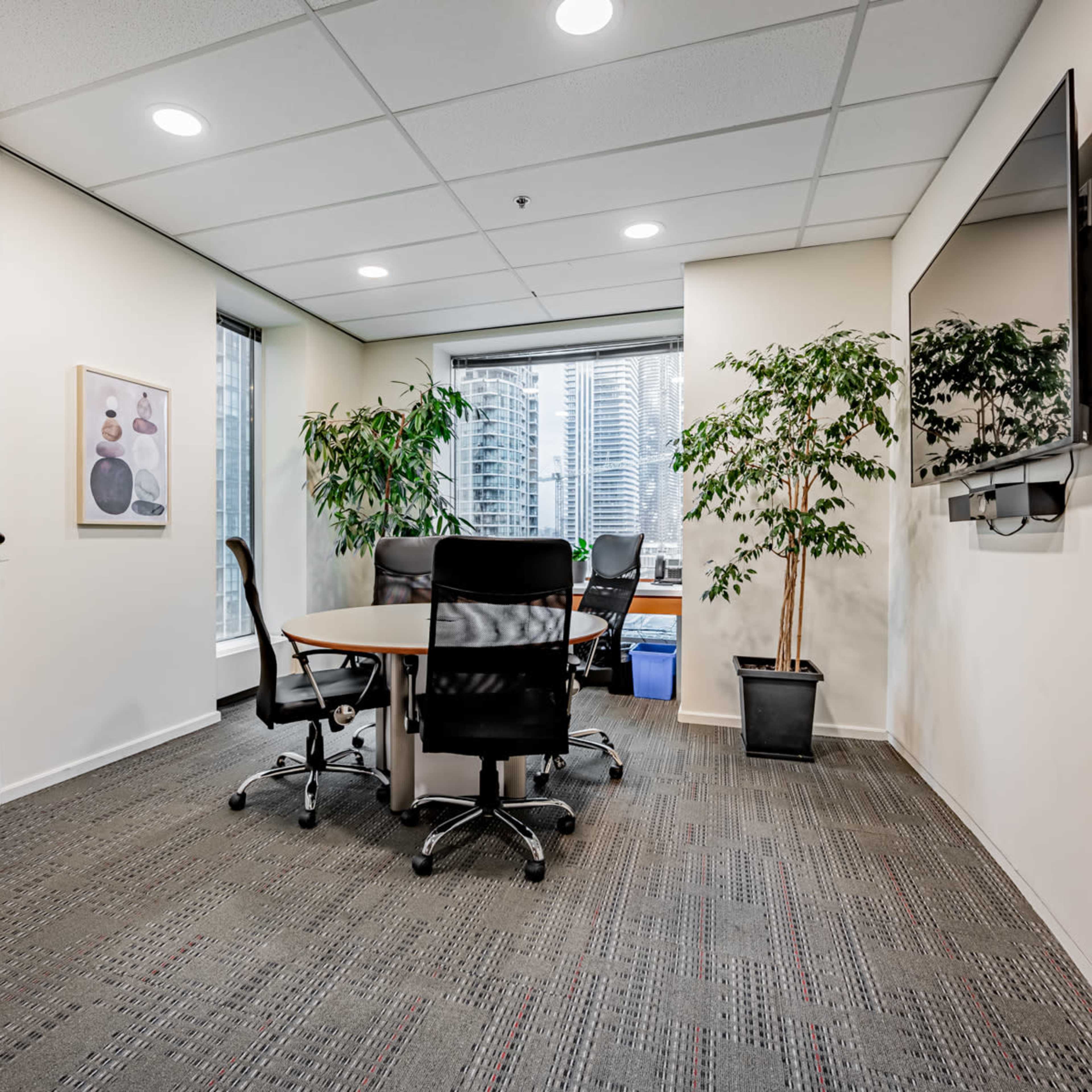 A modern office meeting room with a round table, black chairs, and large windows overlooking a cityscape.