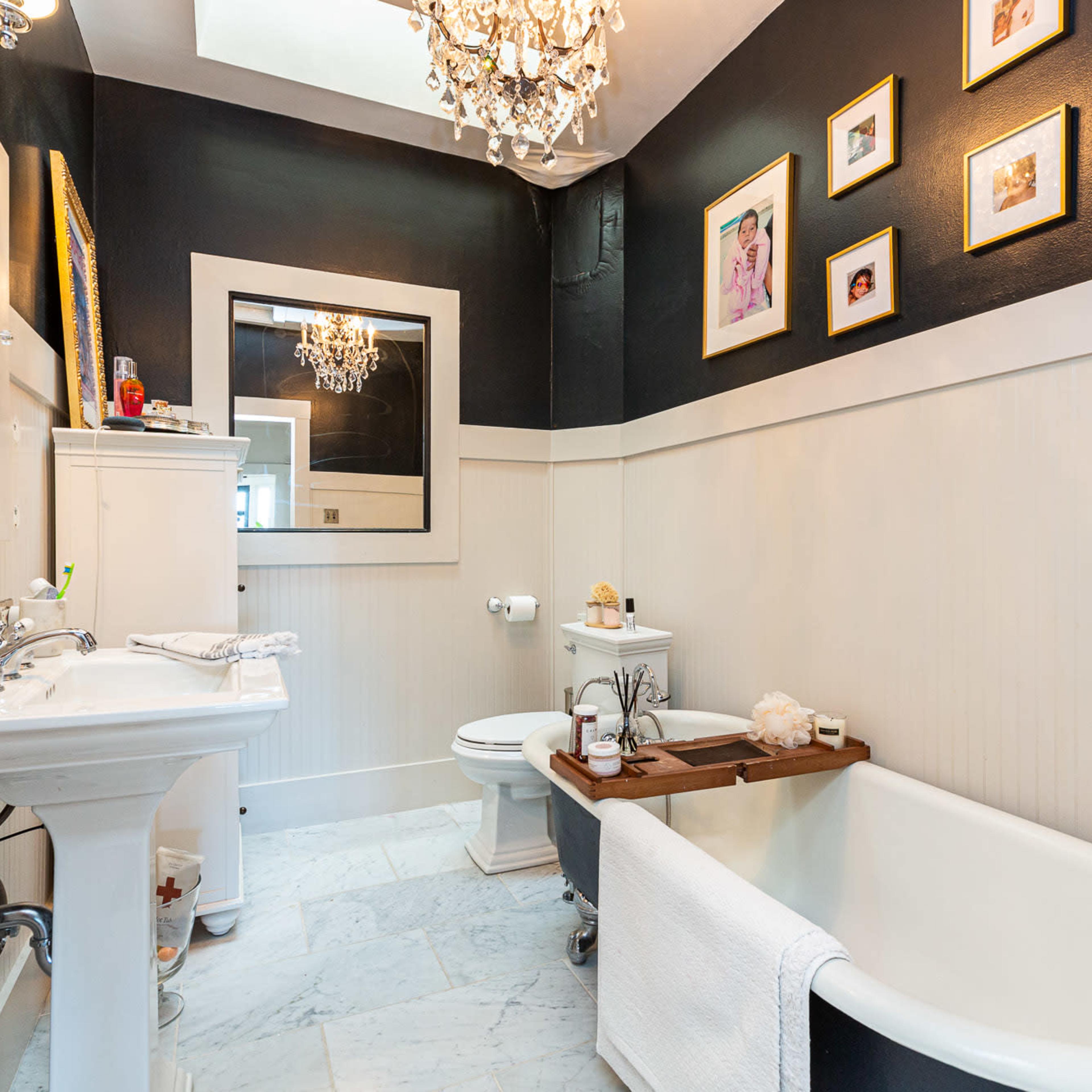 A stylish bathroom featuring a clawfoot bathtub, a modern vanity, elegant light fixtures, and framed pictures on the wall.