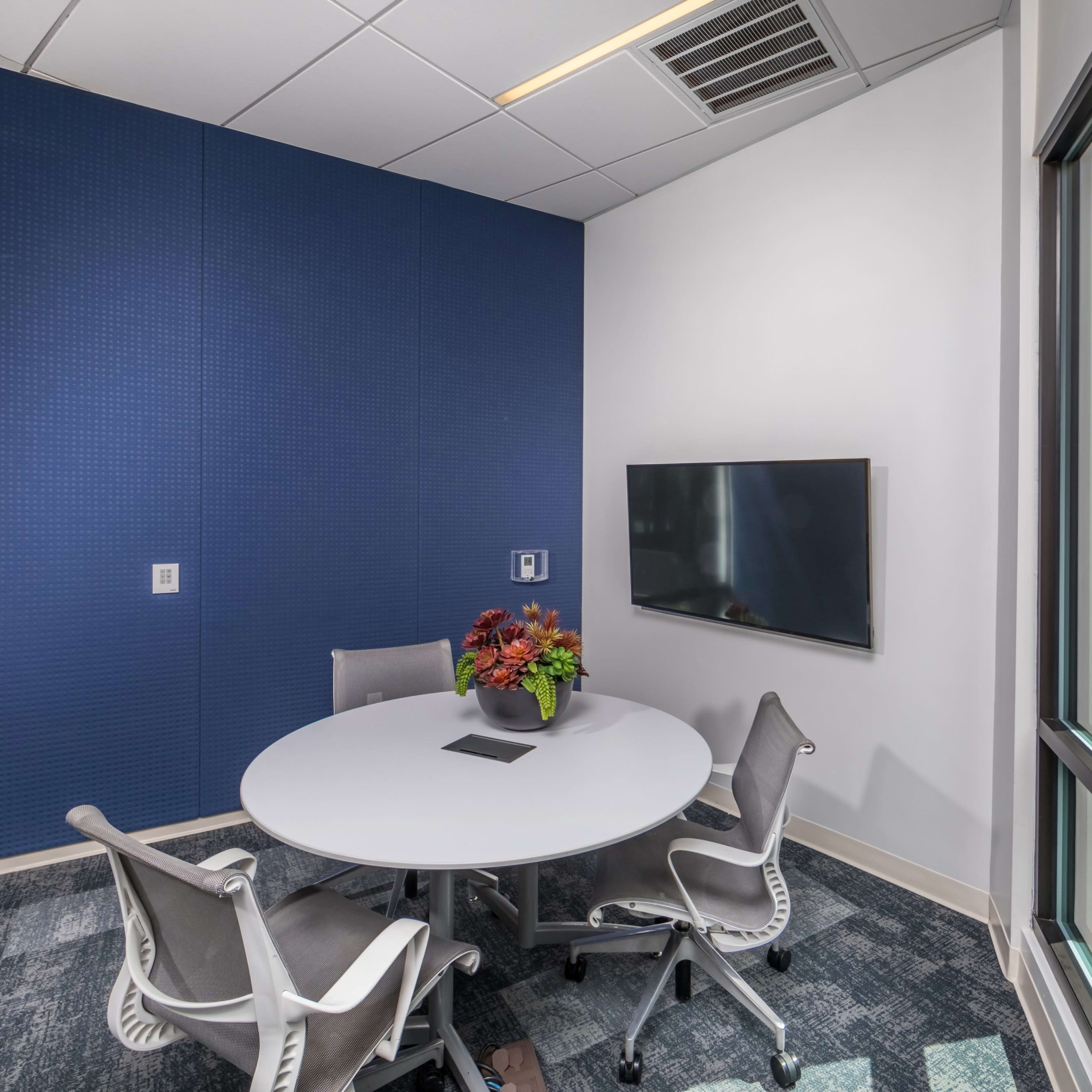 A small conference room features a round table with four chairs and a wall-mounted television.