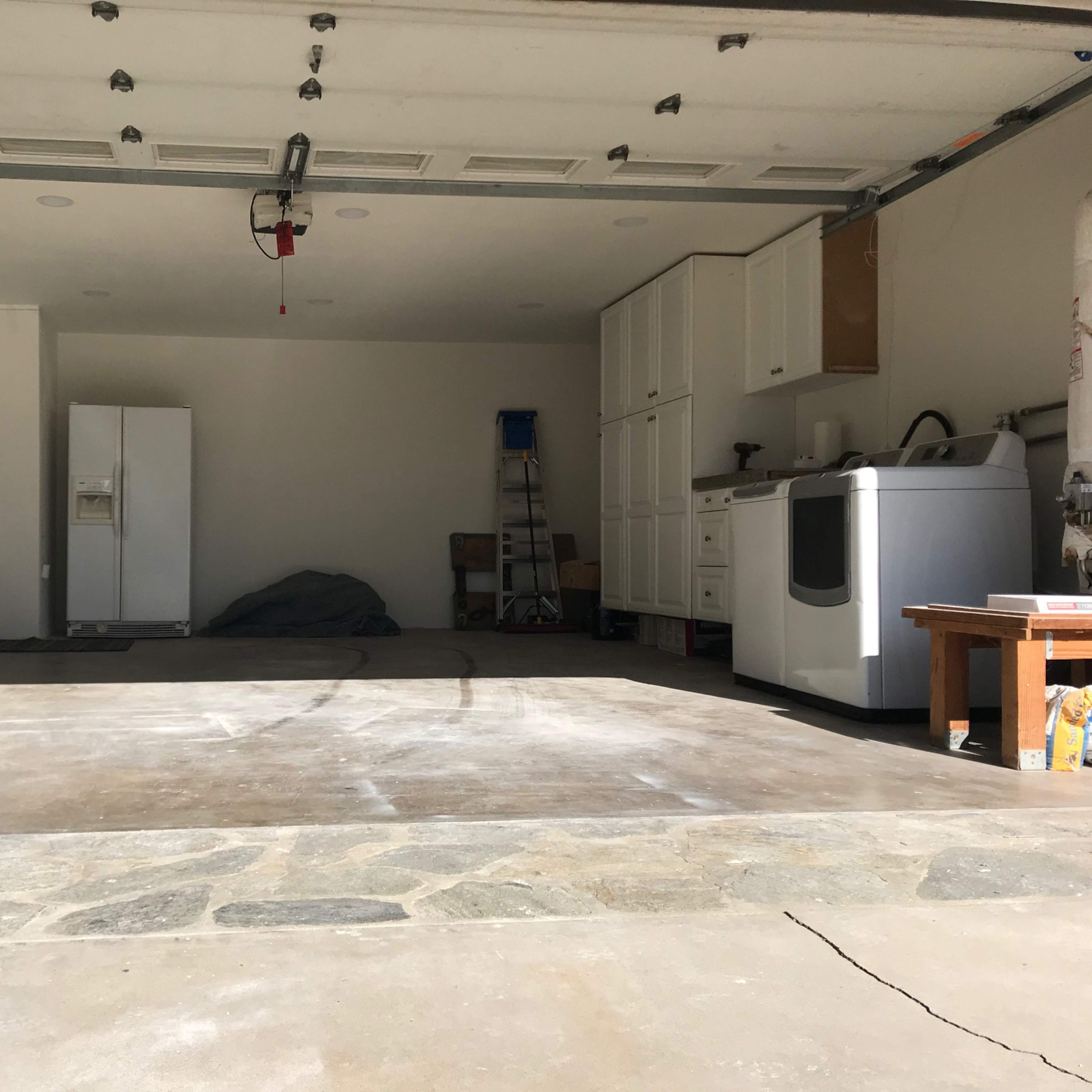 An empty garage with a refrigerator, a washing machine, and storage cabinets along one wall.