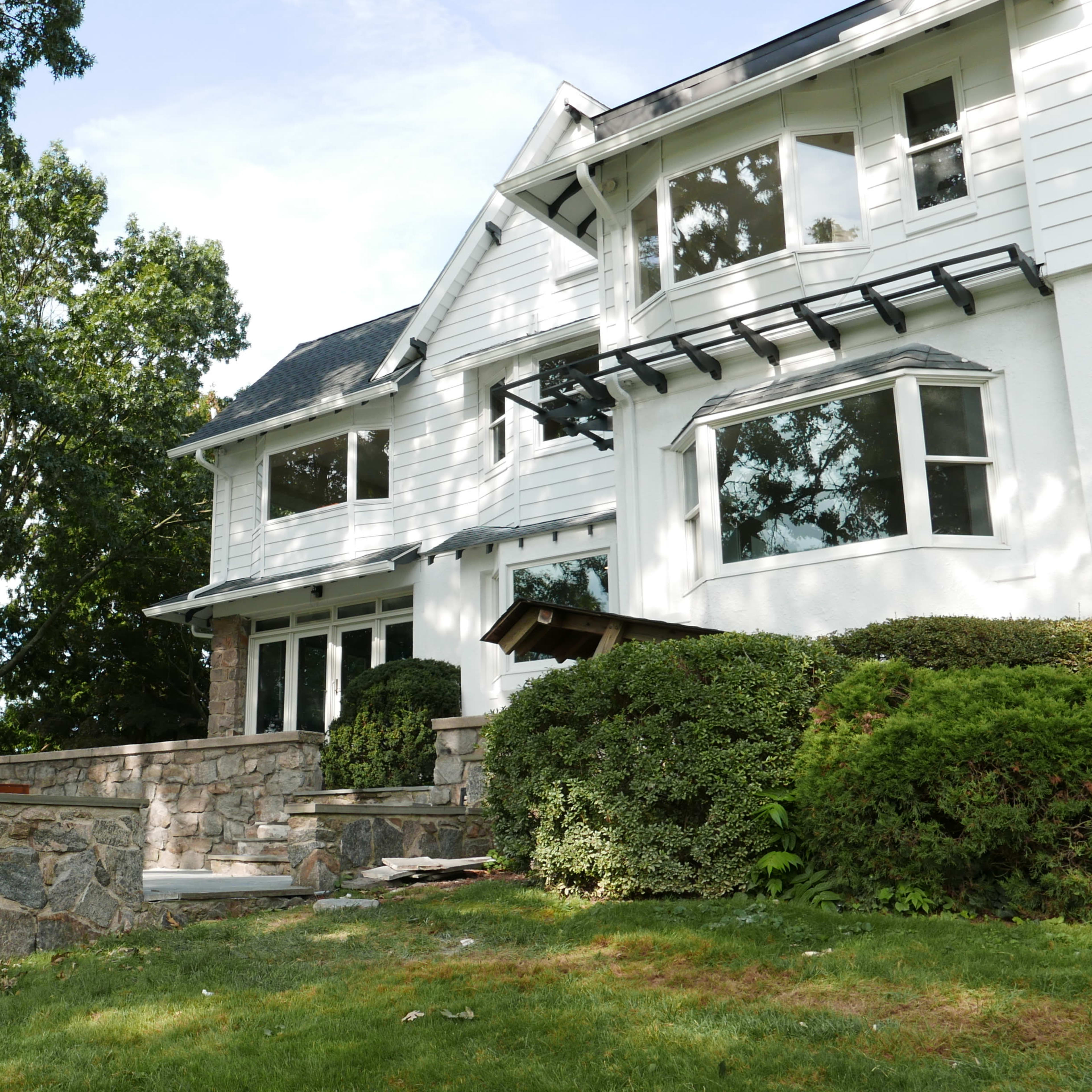 A multi-story house with white siding and stone accents is set on a landscaped yard with green grass and trees.