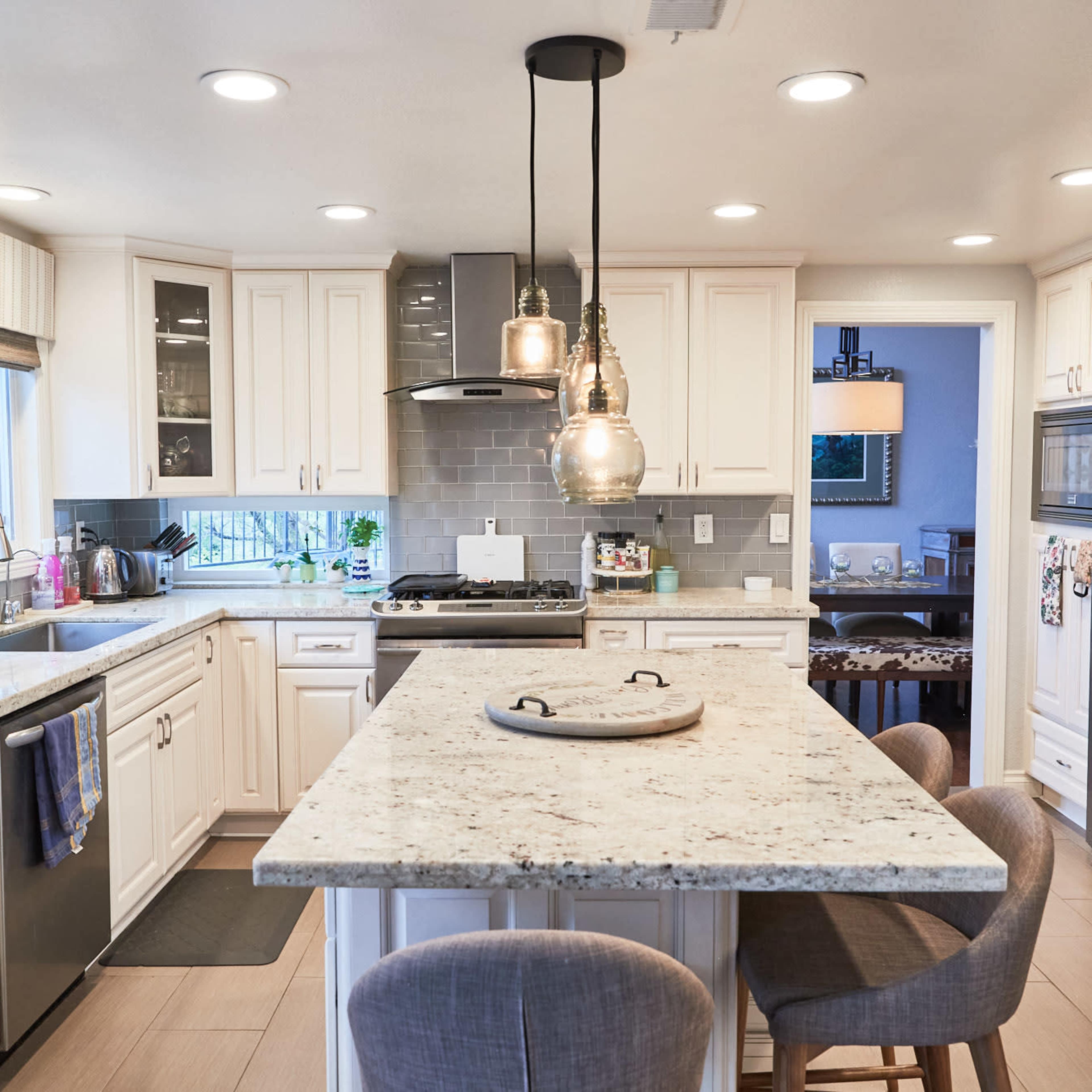 A modern kitchen features white cabinetry, granite countertops, an island with seating, and stainless steel appliances.