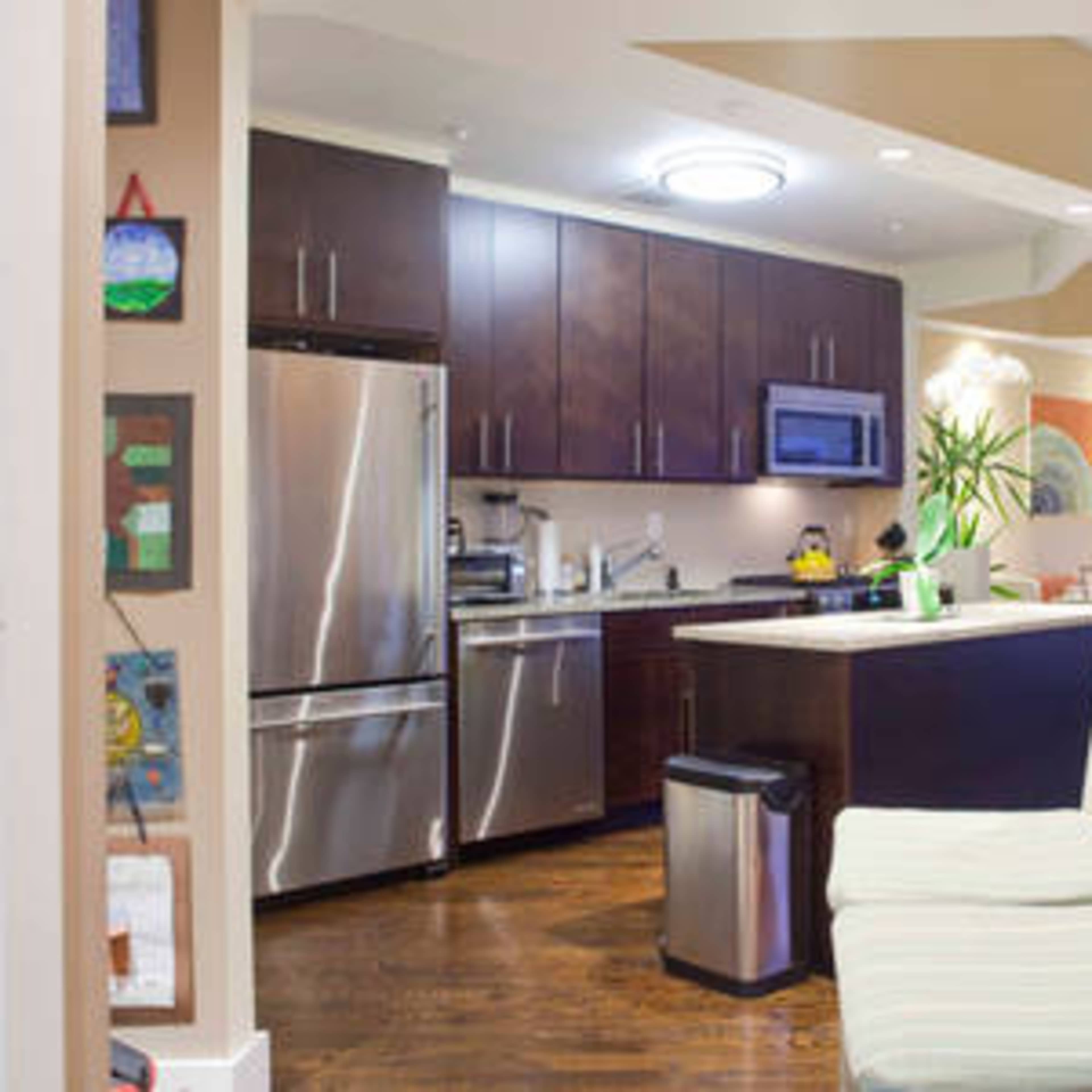 A compact kitchen features dark wood cabinetry, stainless steel appliances, and a small sitting area with a bench.