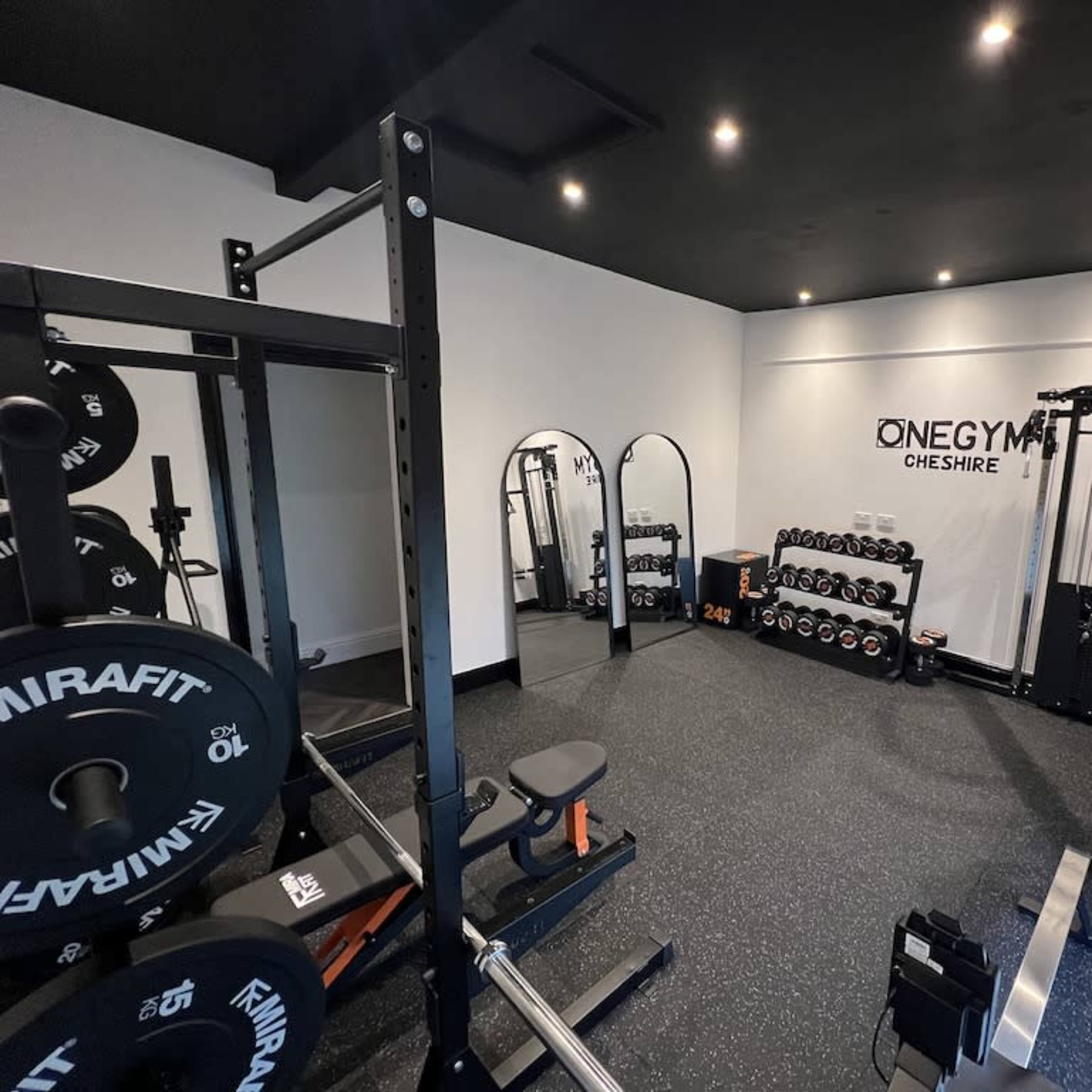 A well-equipped gym with various weightlifting equipment, mirrors, and a selection of dumbbells neatly arranged on a rack.
