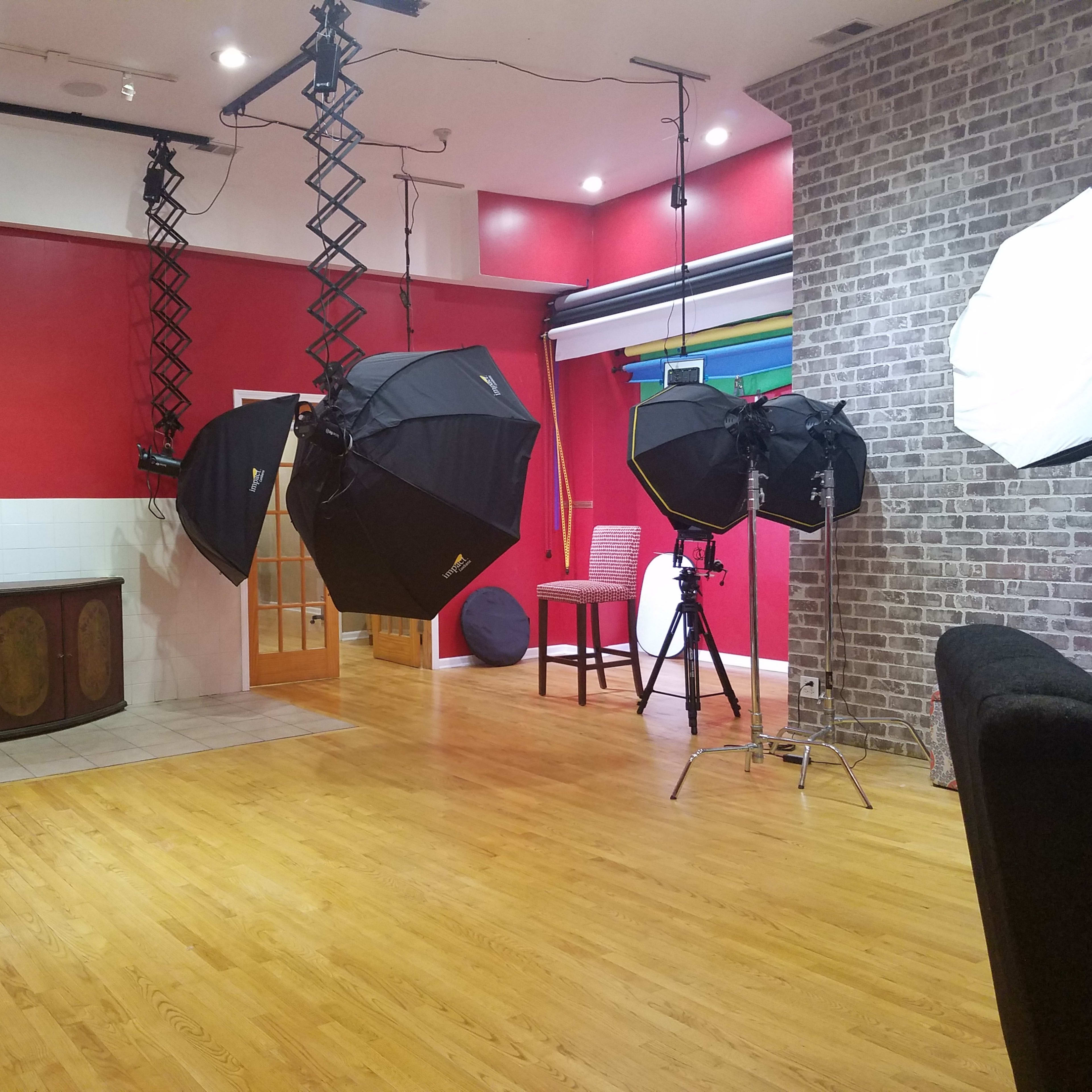 The scene features a photography studio with large softbox lights, a brick wall, and wooden flooring, alongside various furniture pieces.