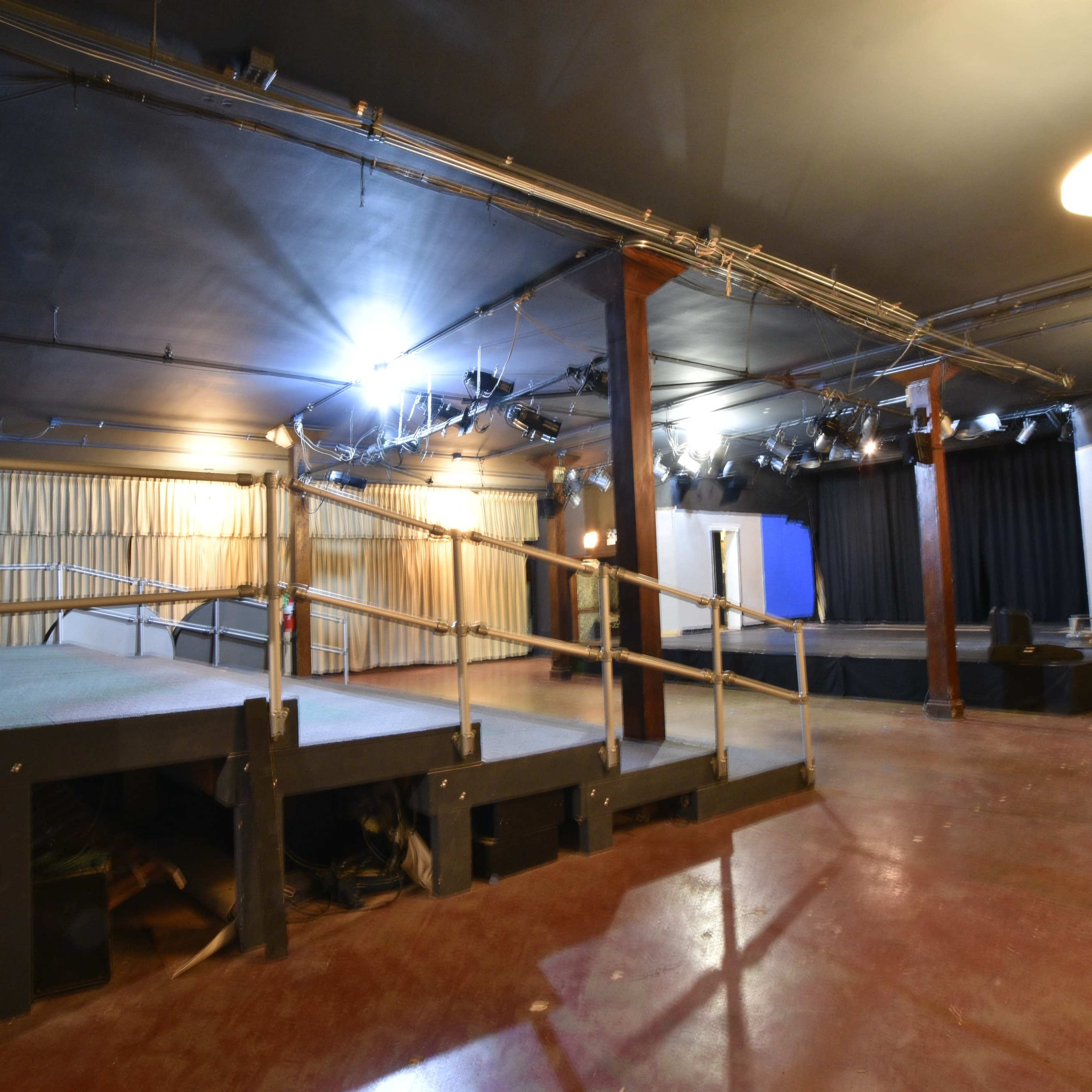 An empty performance space with staging areas, lighting rigging, and curtains along the walls.
