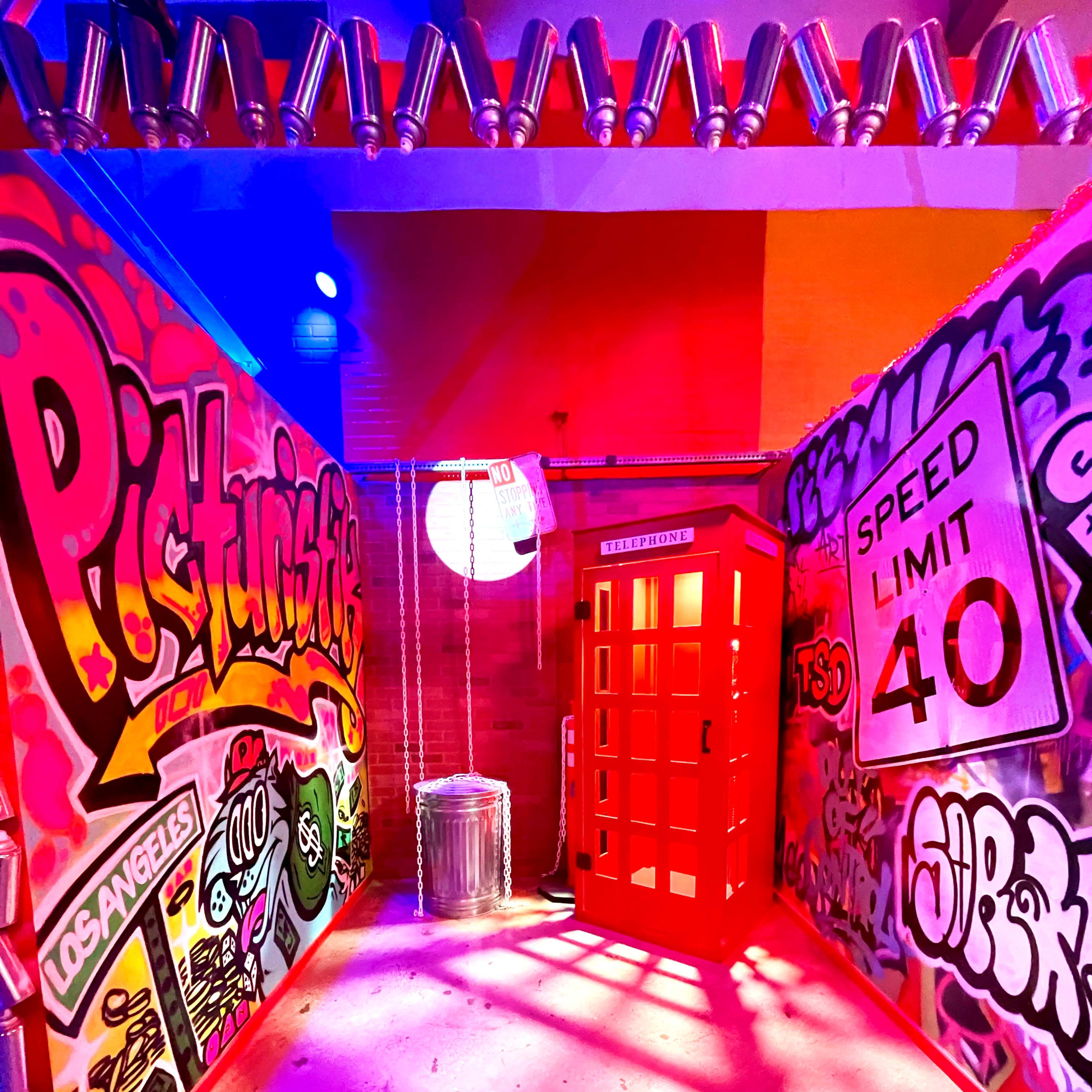 A brightly lit alleyway adorned with colorful graffiti on the walls, featuring a red telephone booth in the center.