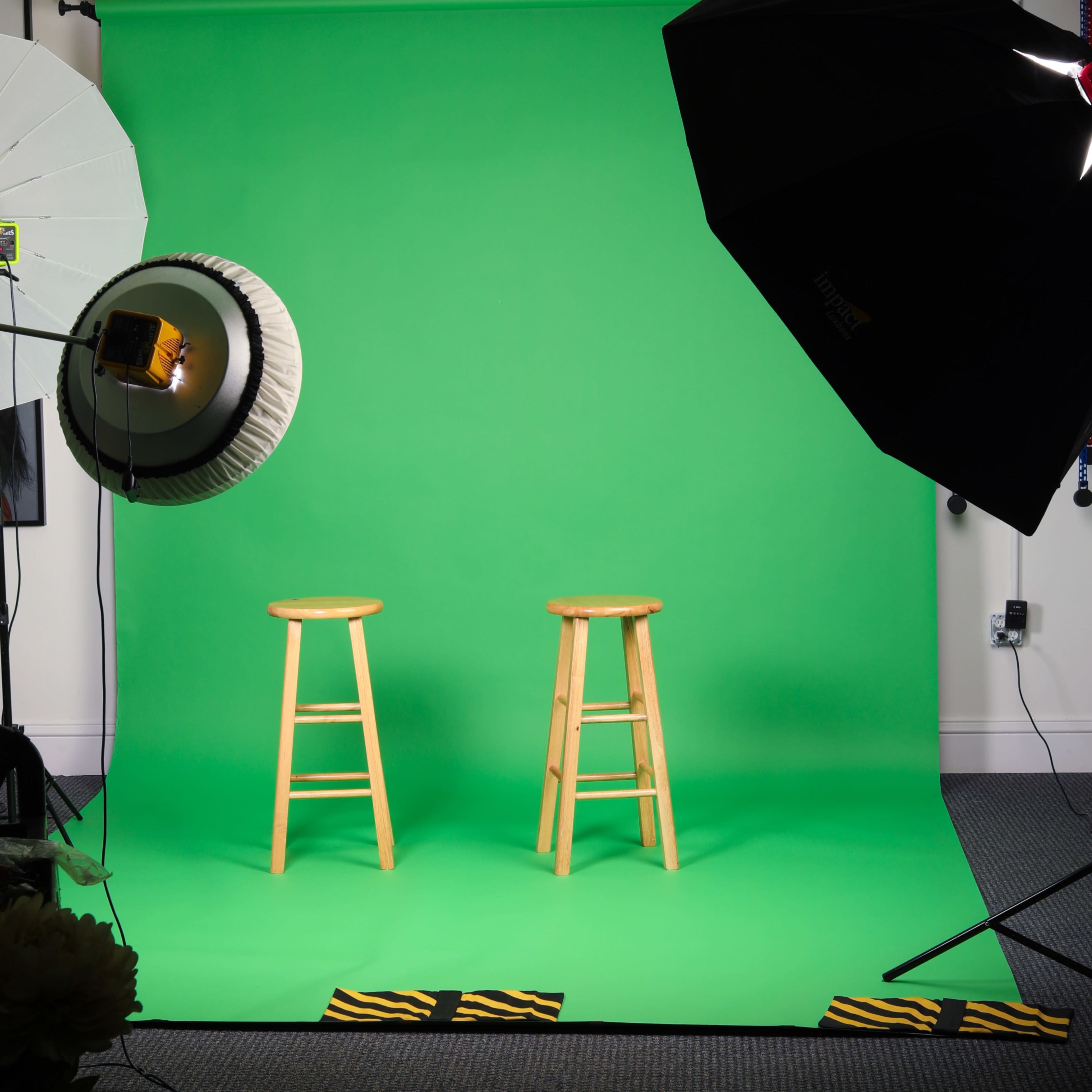 Two wooden stools placed in front of a green screen, with studio lights positioned to illuminate the scene.
