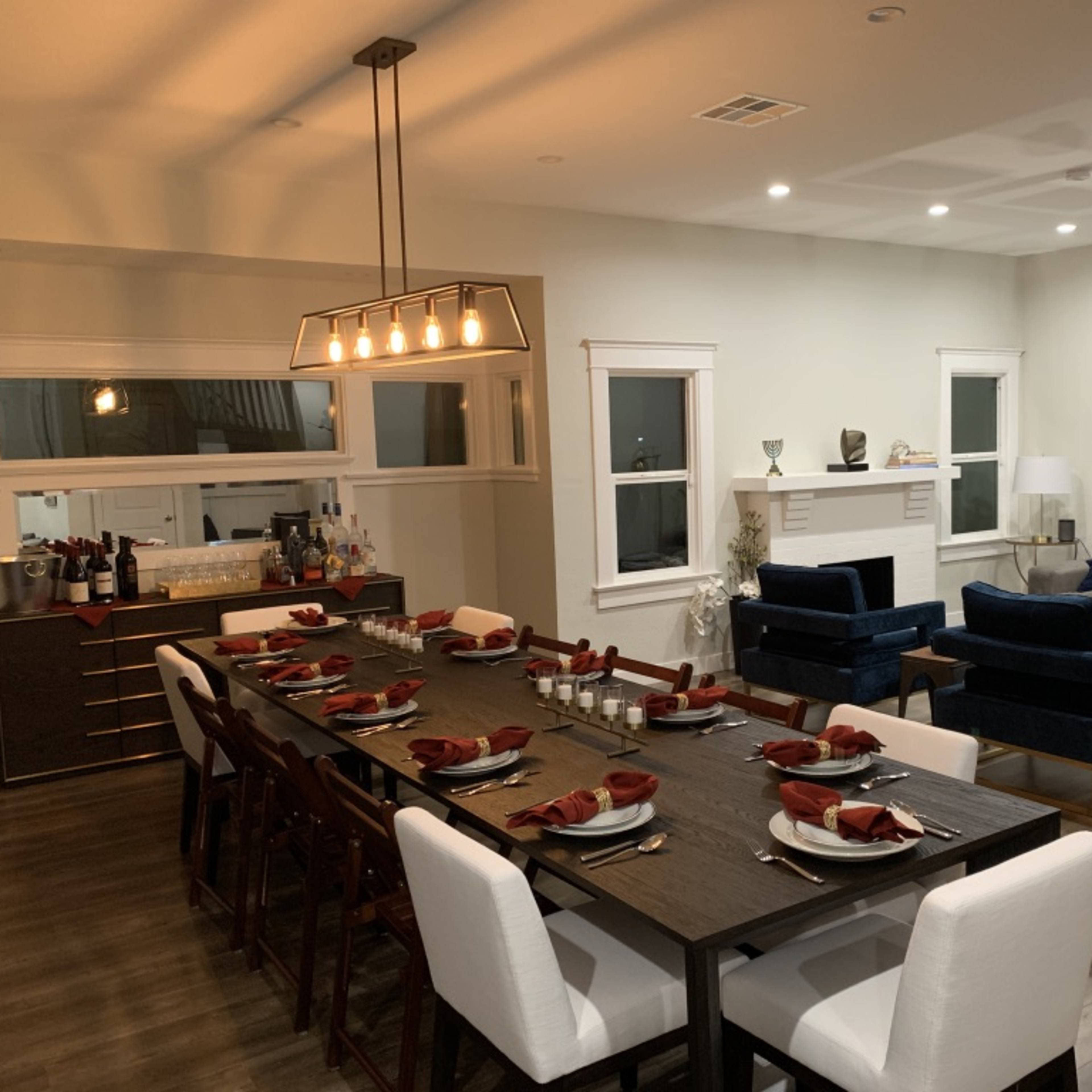 A spacious dining area features a long table set with red napkins and an adjacent seating area with two blue couches.