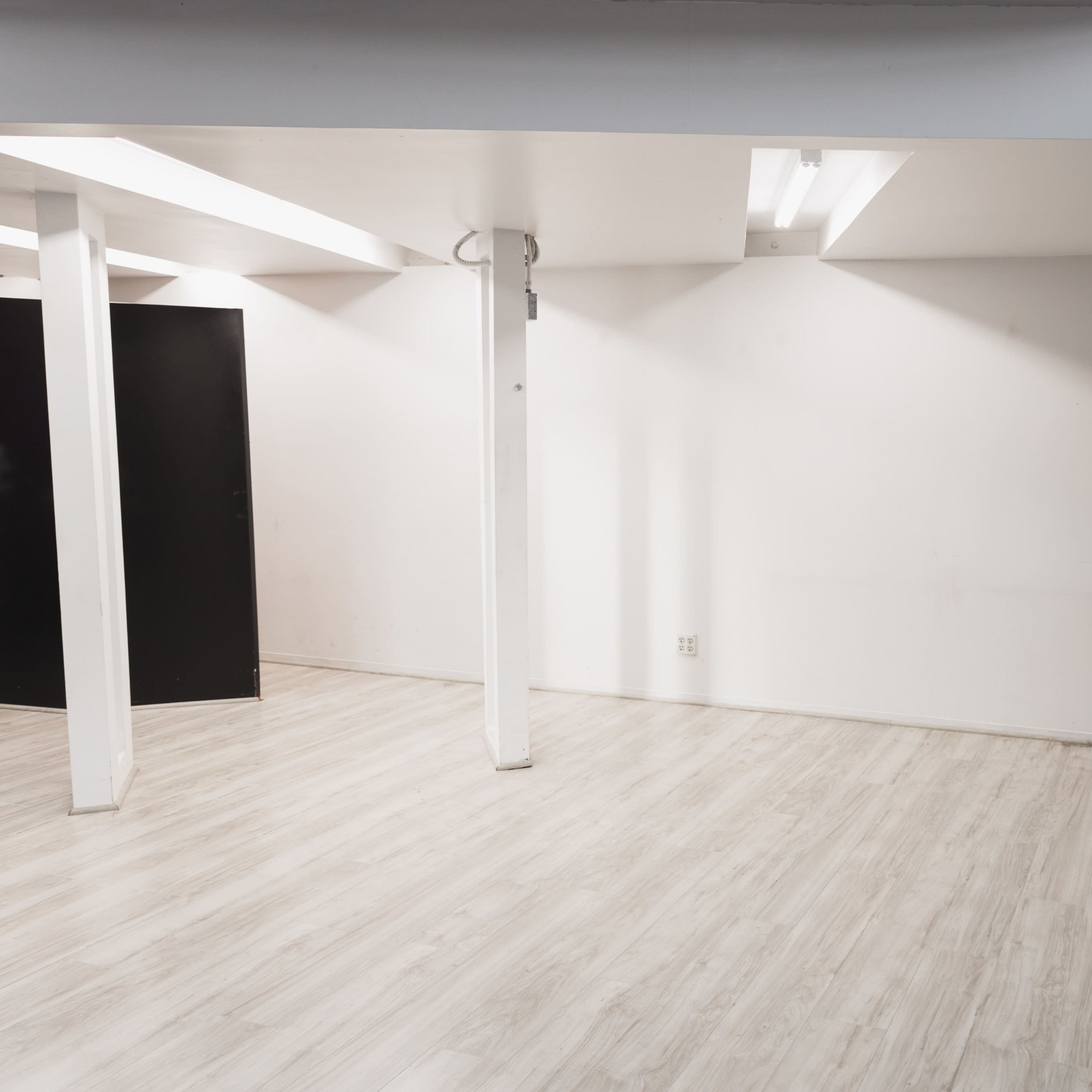 An empty room with polished light wooden flooring, white walls, and a black door on one side.