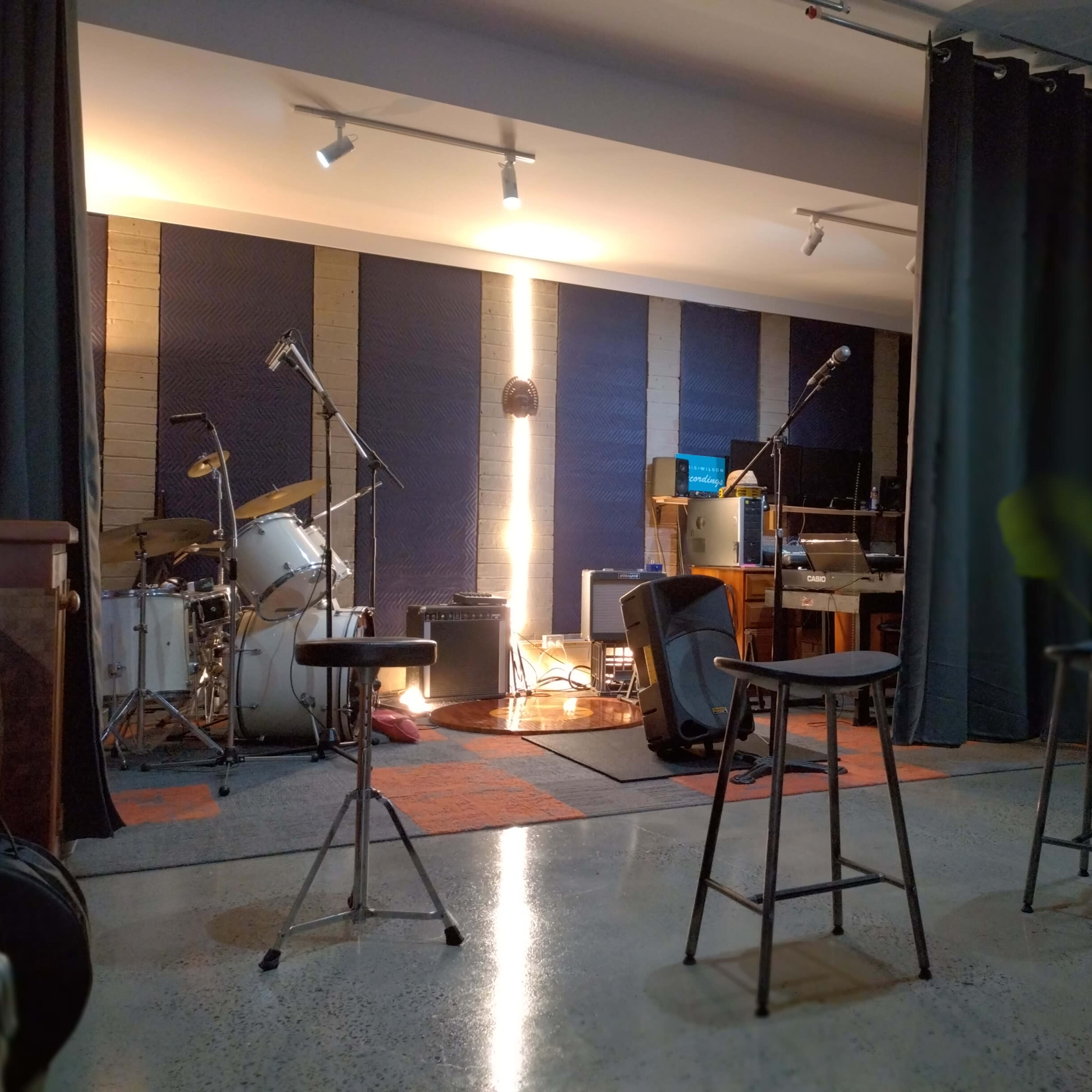 A music studio with a drum set, microphones, and various instruments arranged in a well-lit space.