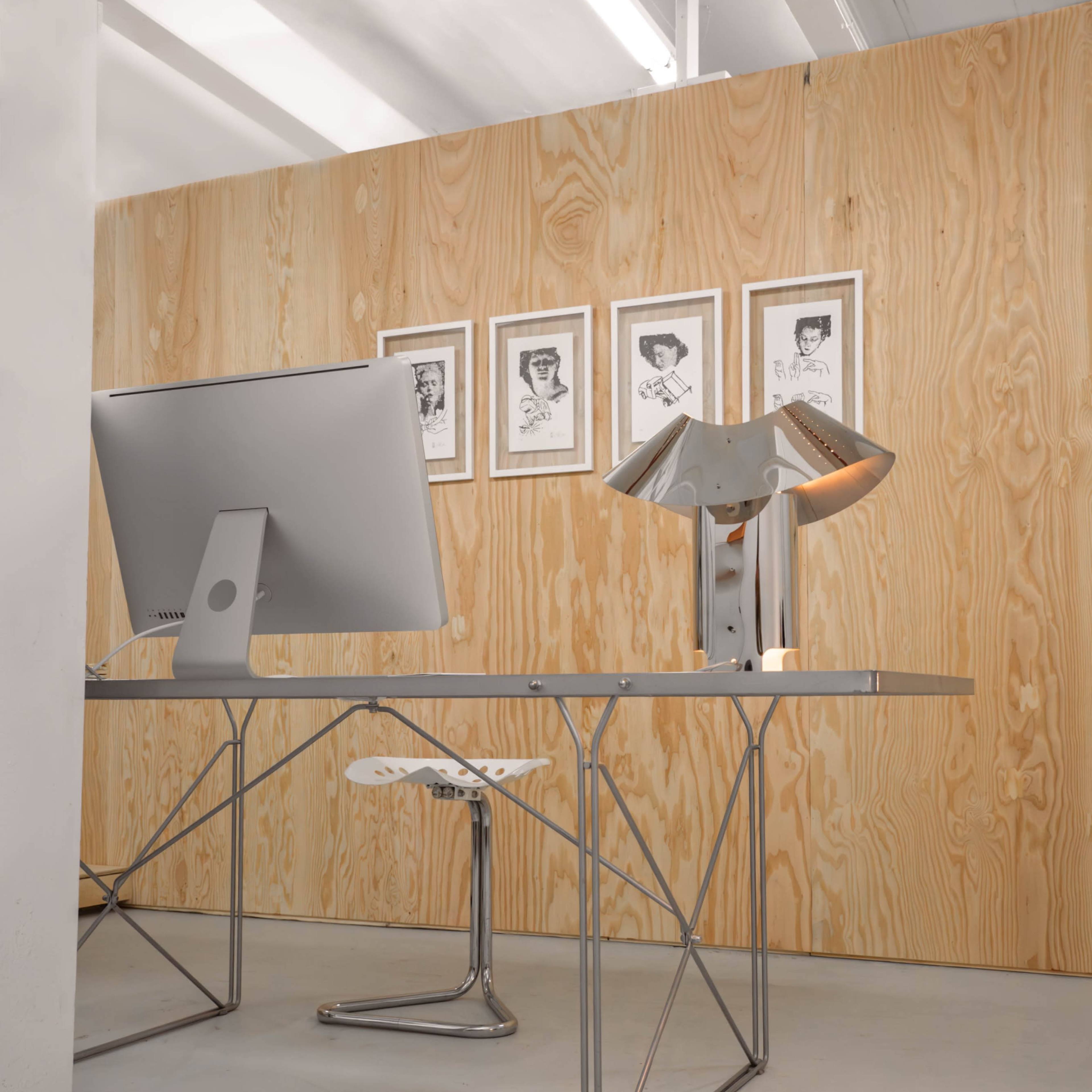 A modern office space features a sleek desk with a computer, a unique lamp, and framed artworks on a wooden wall.