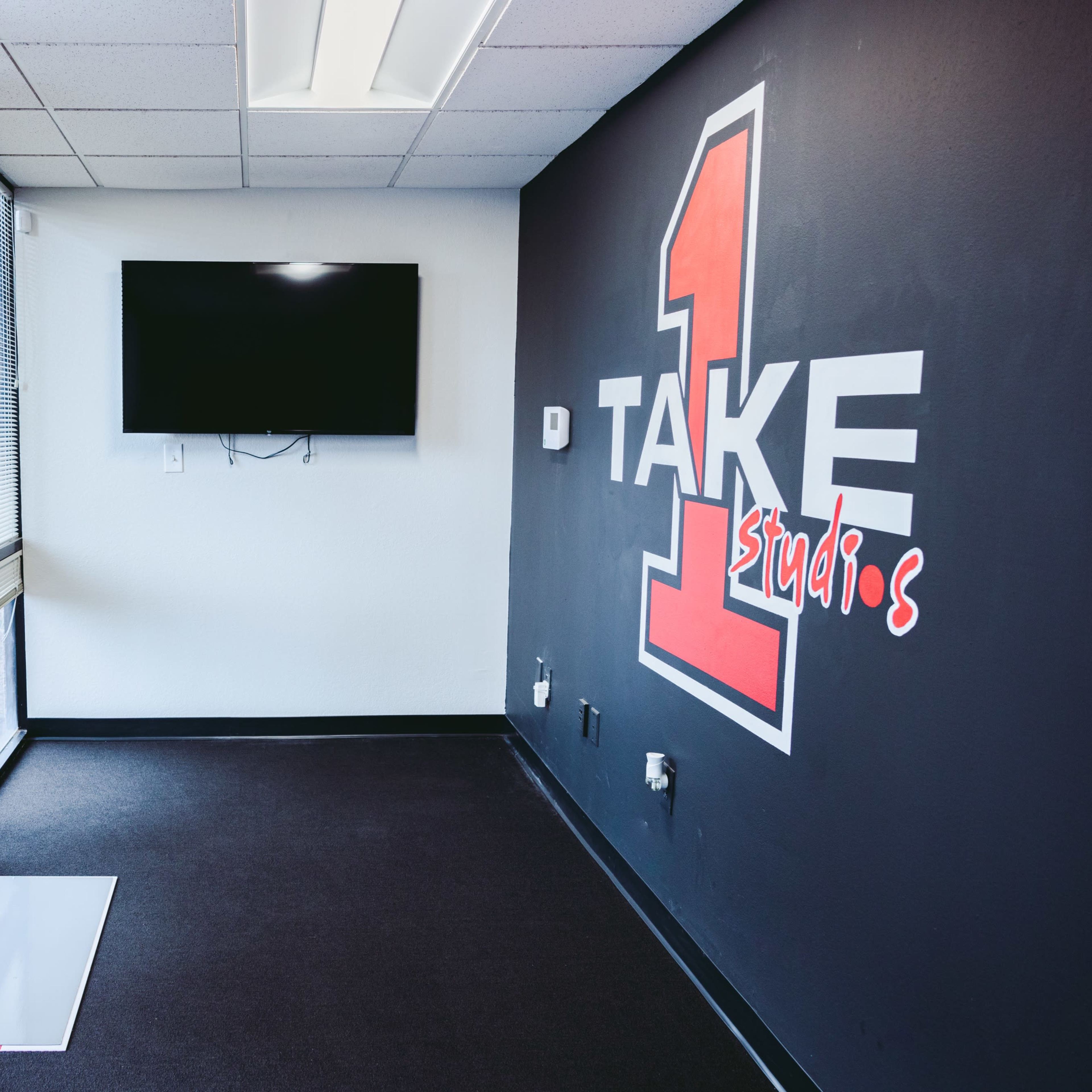 A corner of an interior room featuring a large wall with the text "TAKE 1 studios" and a mounted flat-screen TV.