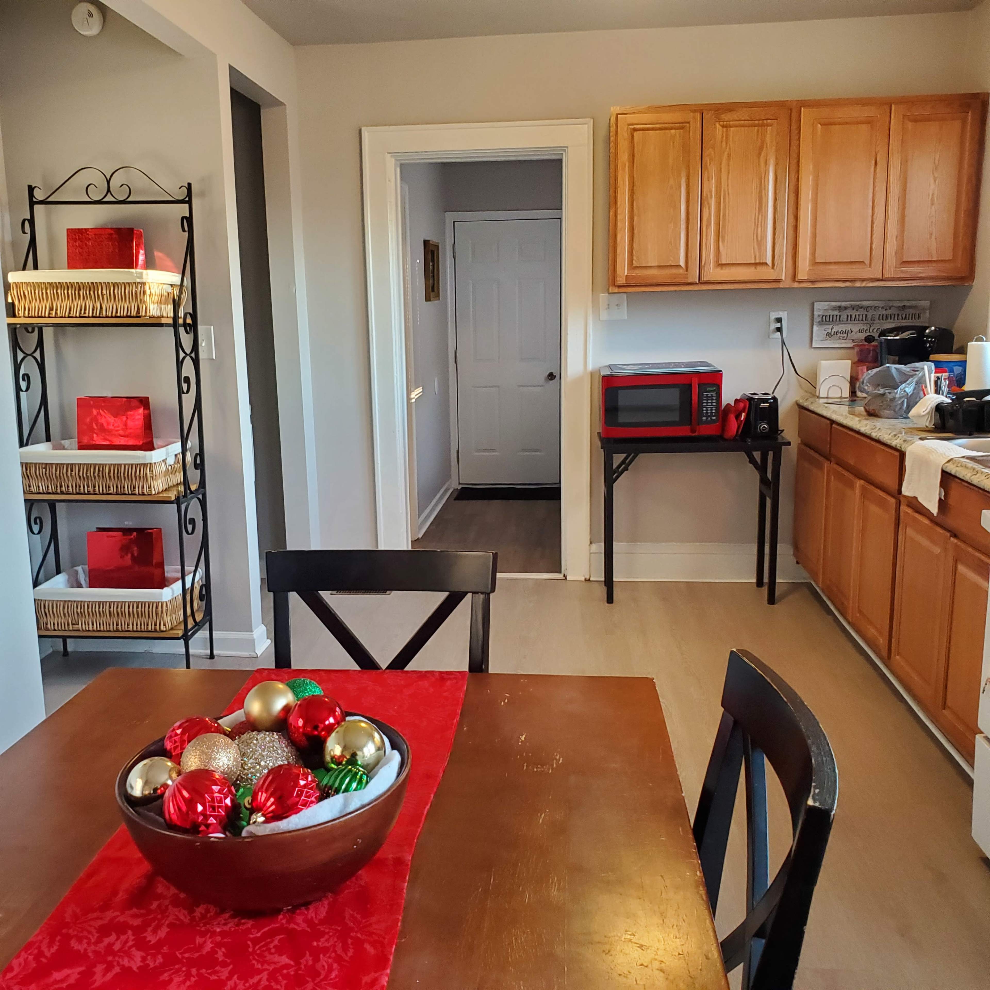 A kitchen area featuring a dining table with a decorative bowl of ornaments, wooden cabinets, and a microwave on the counter.