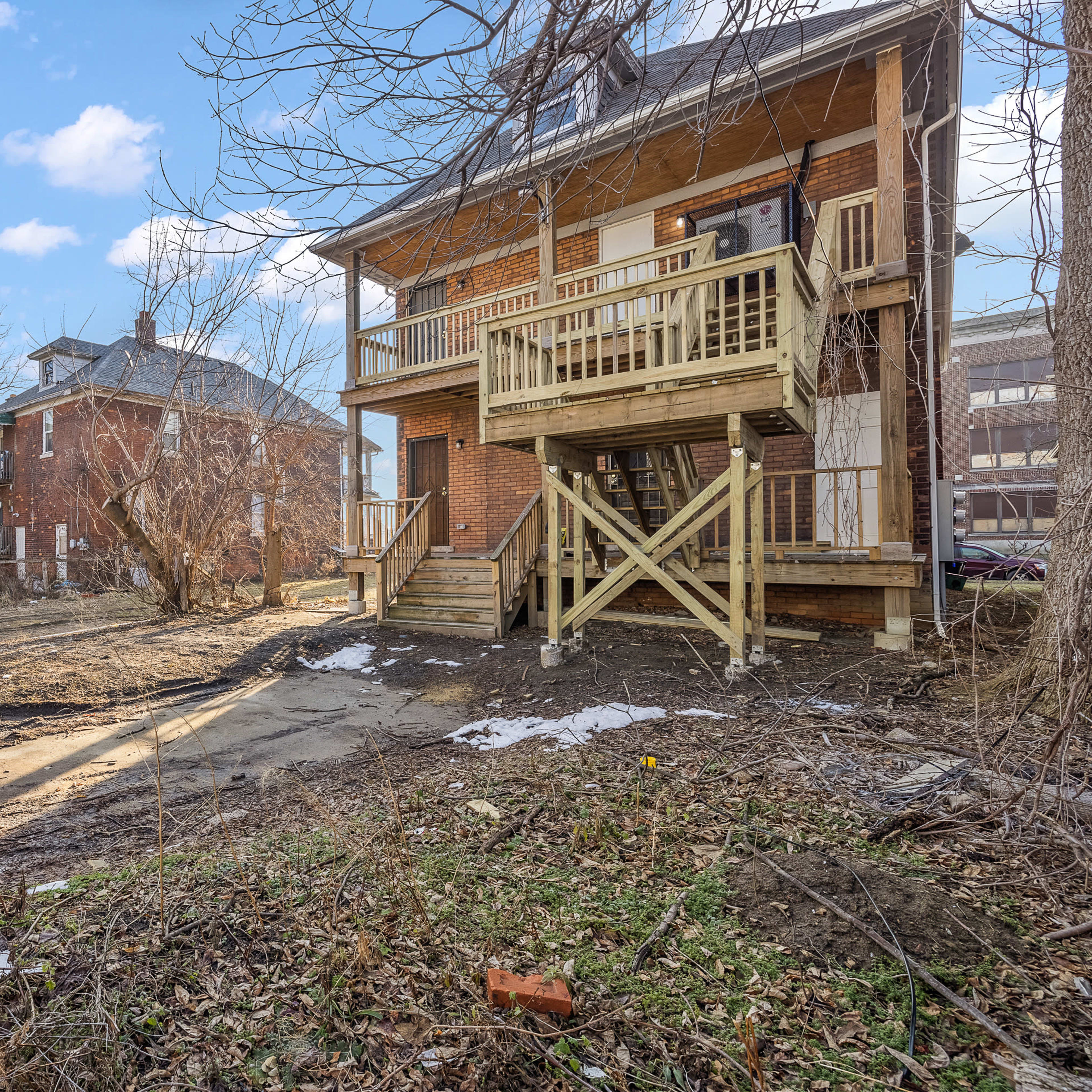 A vacant lot with overgrown vegetation is located beside a two-story building with a wooden deck and staircase.