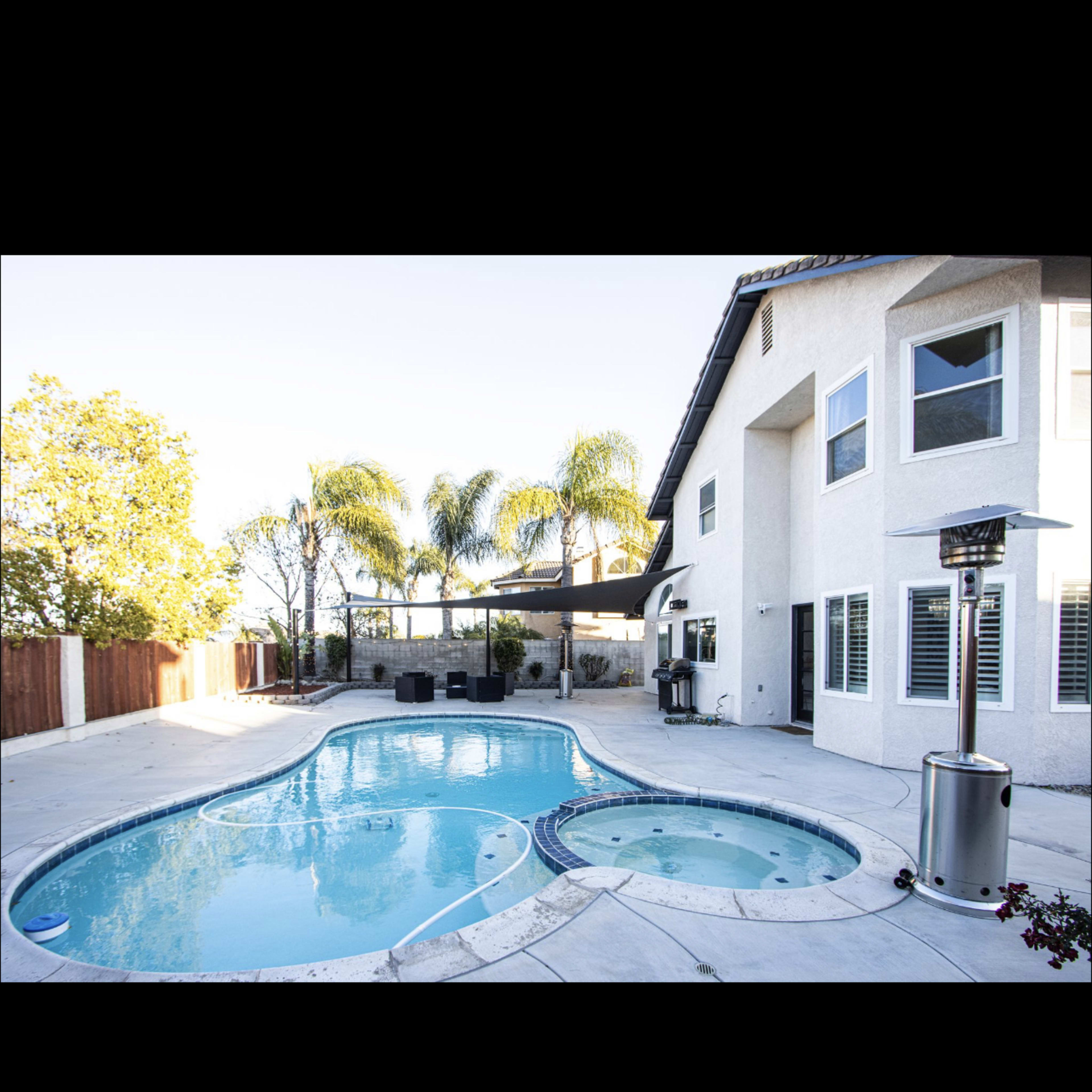 A residential backyard with a swimming pool and spa surrounded by palm trees and a well-maintained patio.