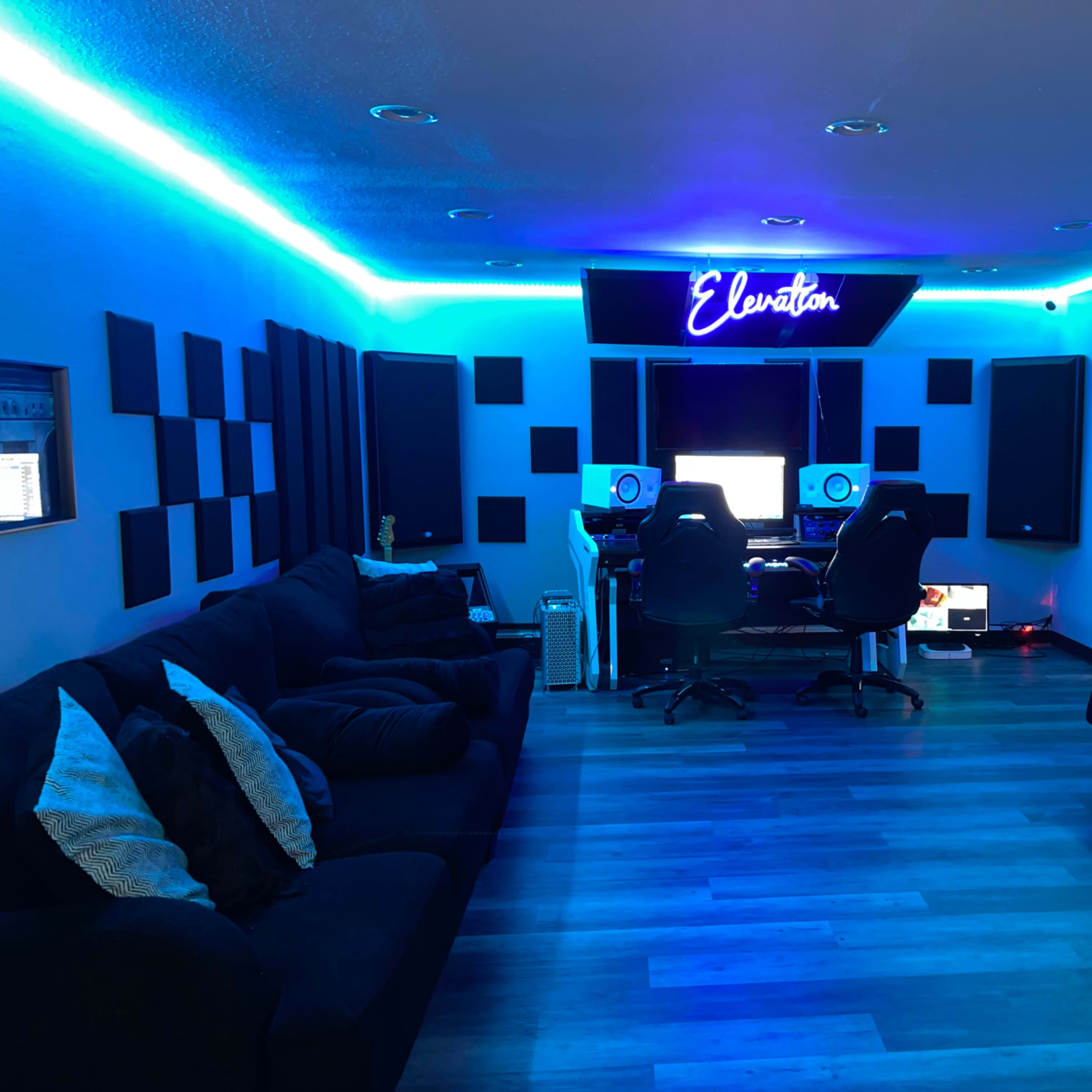 A music studio with blue LED lighting, padded walls, and a central workstation equipped with monitors and audio equipment.