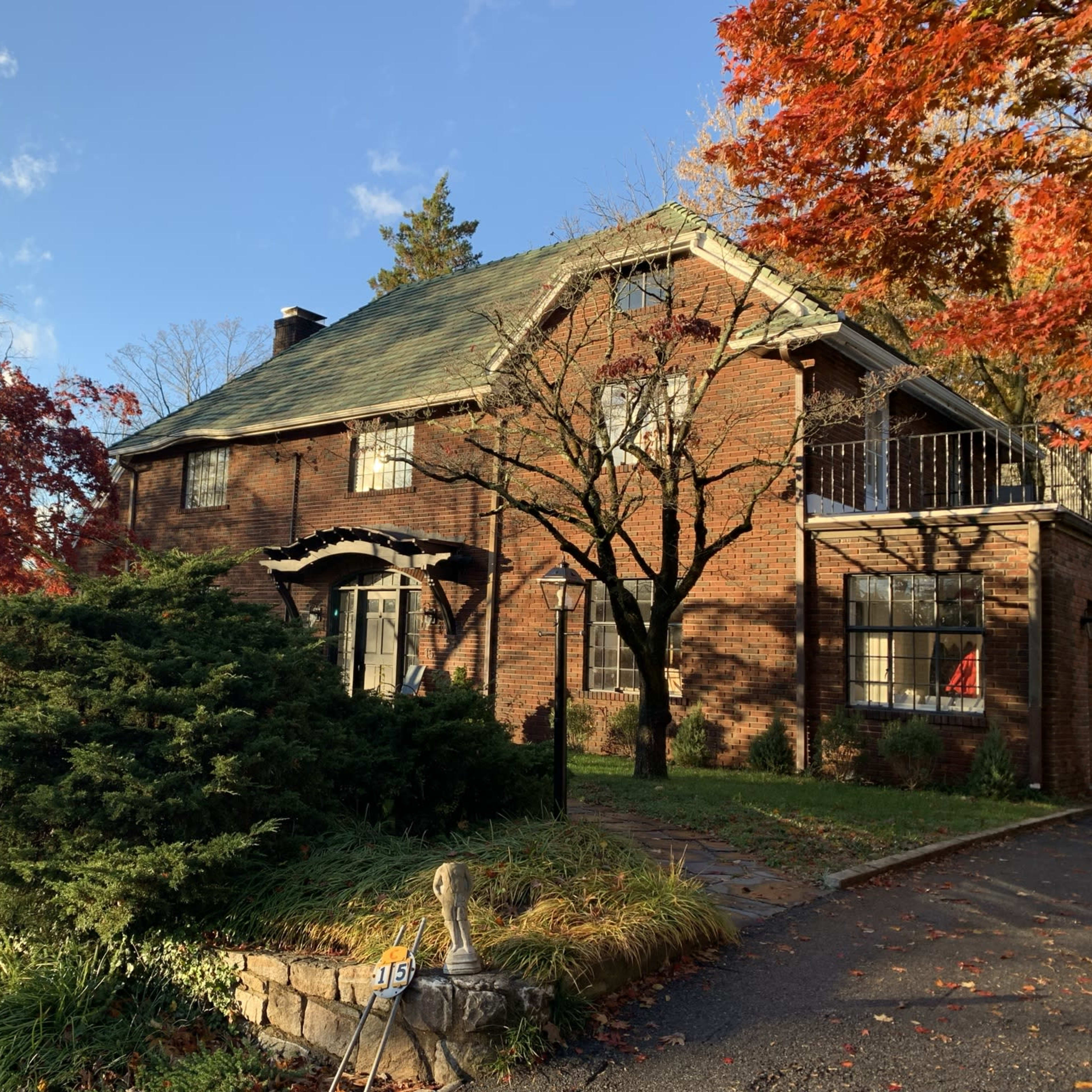 A brick house with a sloped roof is surrounded by colorful autumn foliage and greenery.