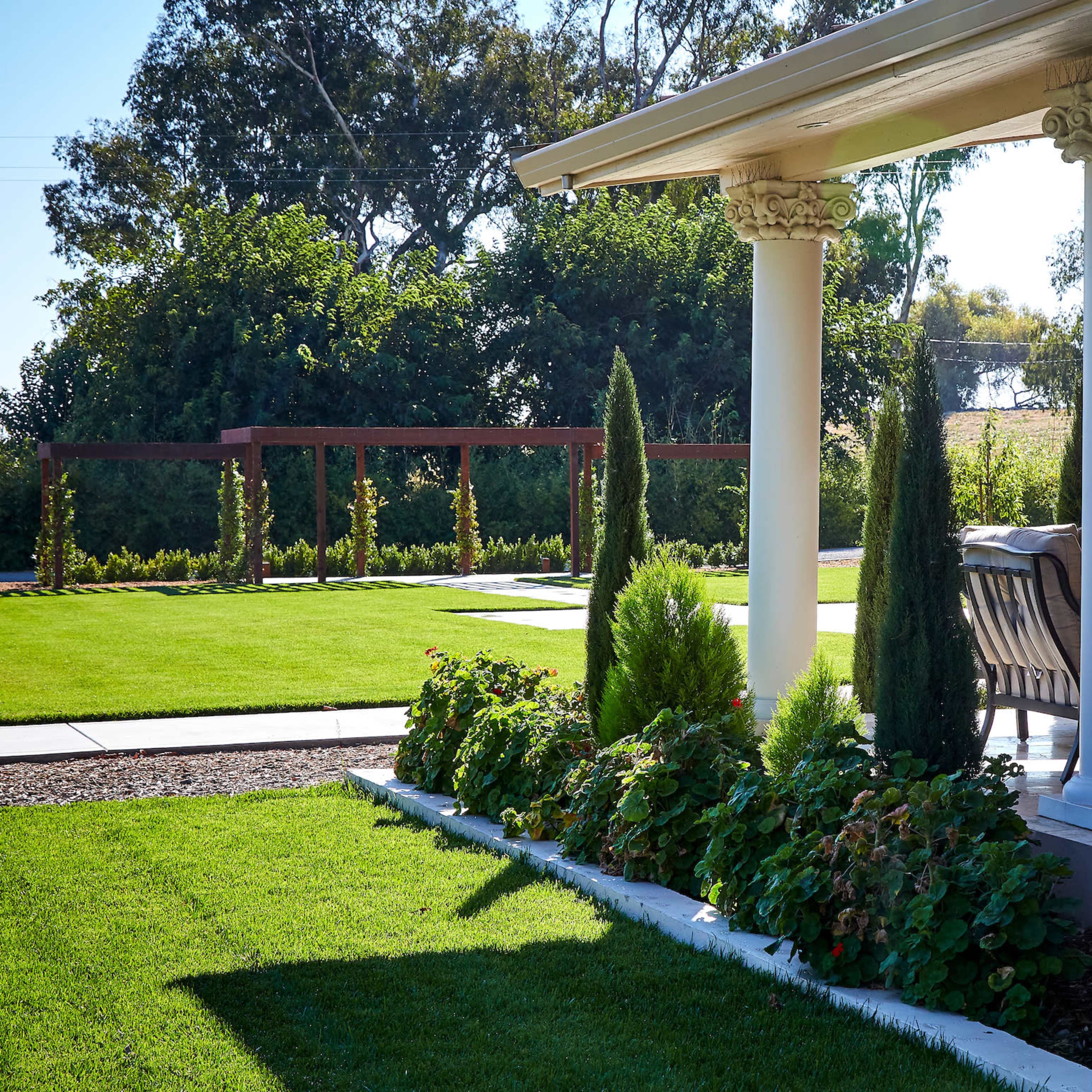 A landscaped patio area featuring columns, stone walls, and neatly trimmed hedges under a clear sky.