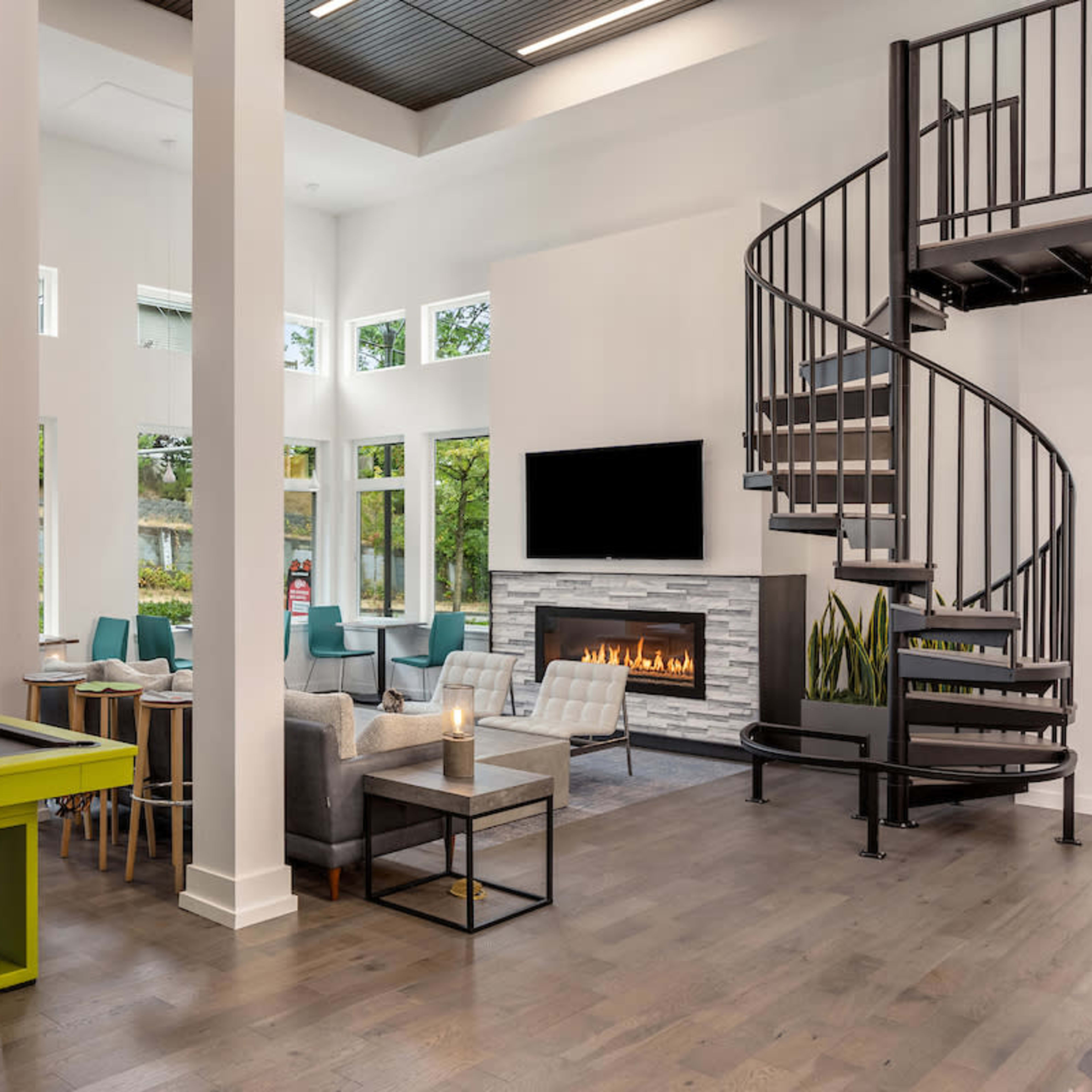 A modern common area featuring a pool table, spiral staircase, a fireplace, and large windows that allow natural light to fill the space.