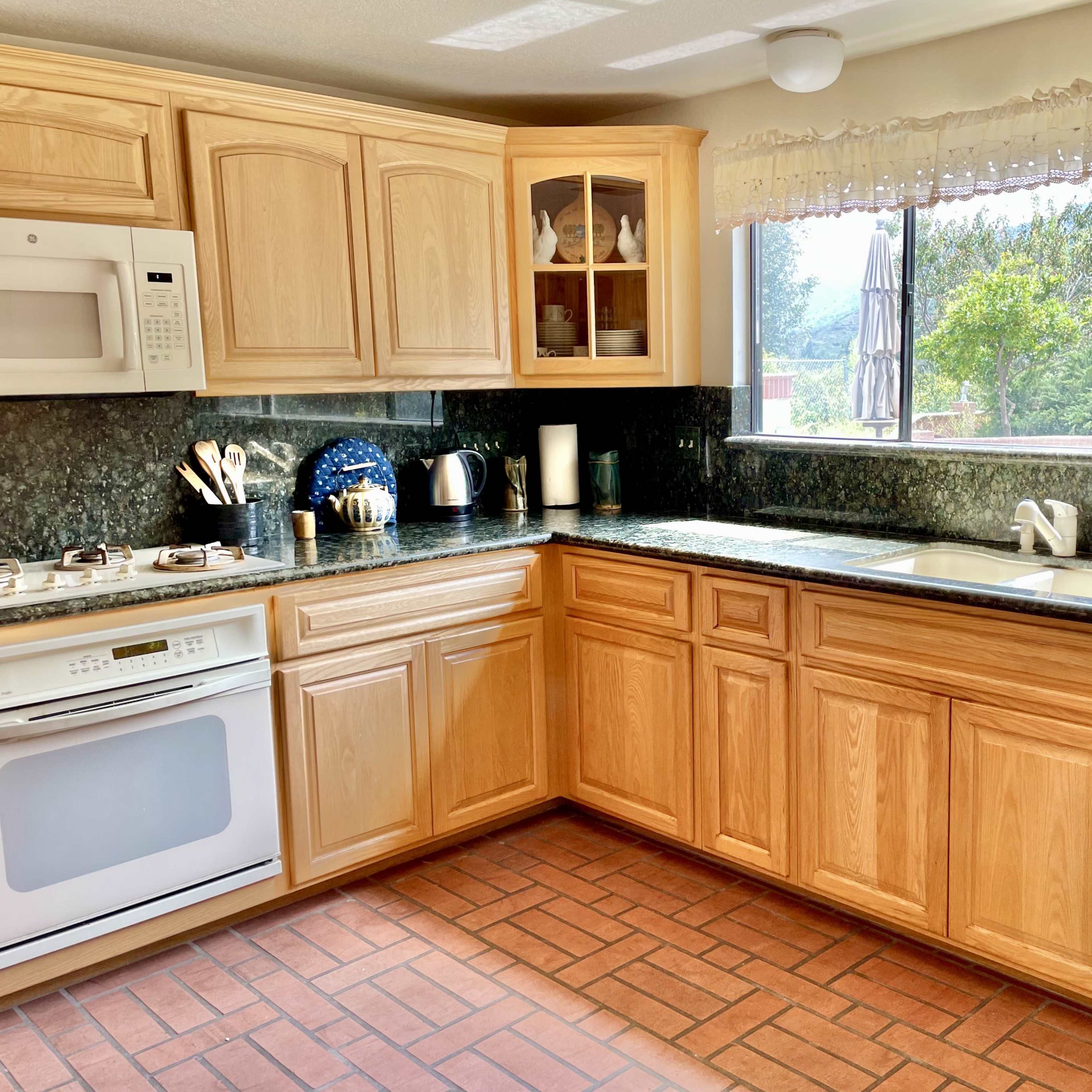 A modern kitchen features wooden cabinets, a granite countertop, and a window overlooking greenery.