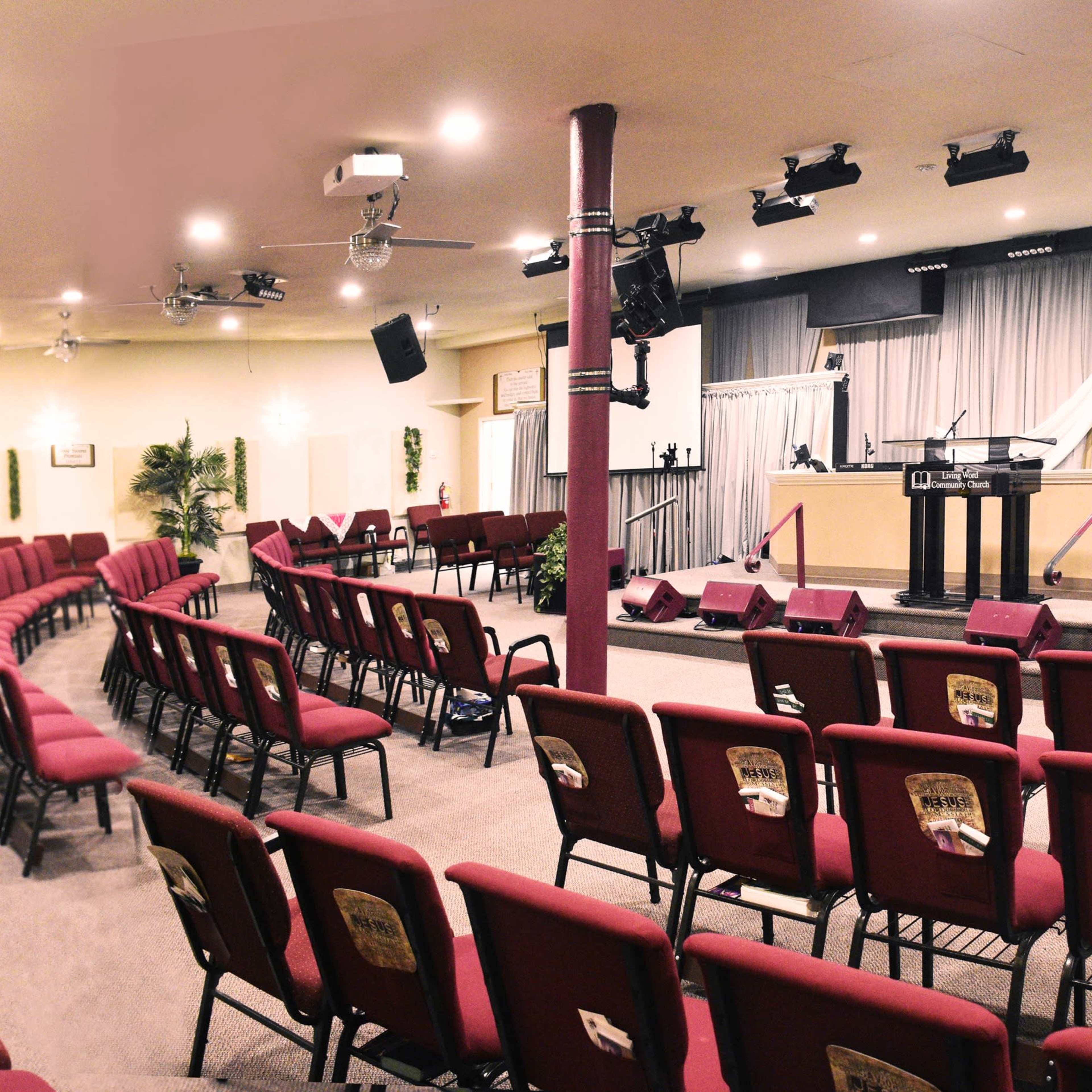 A church interior with red chairs arranged in a semicircular layout facing a stage.