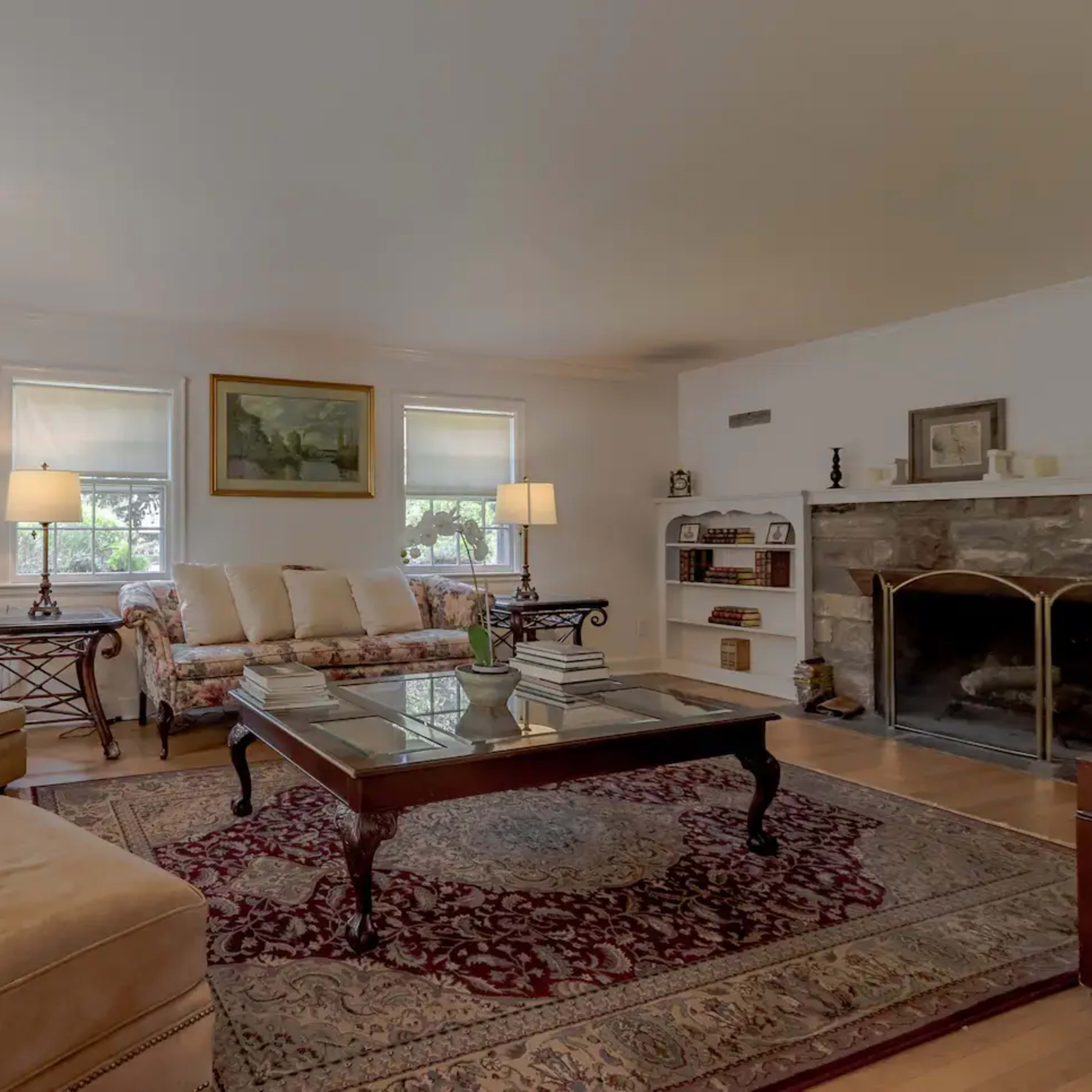 The living room features a cream-colored sofa and an armchair, a wooden coffee table, a stone fireplace, and light-colored walls with framed artwork.