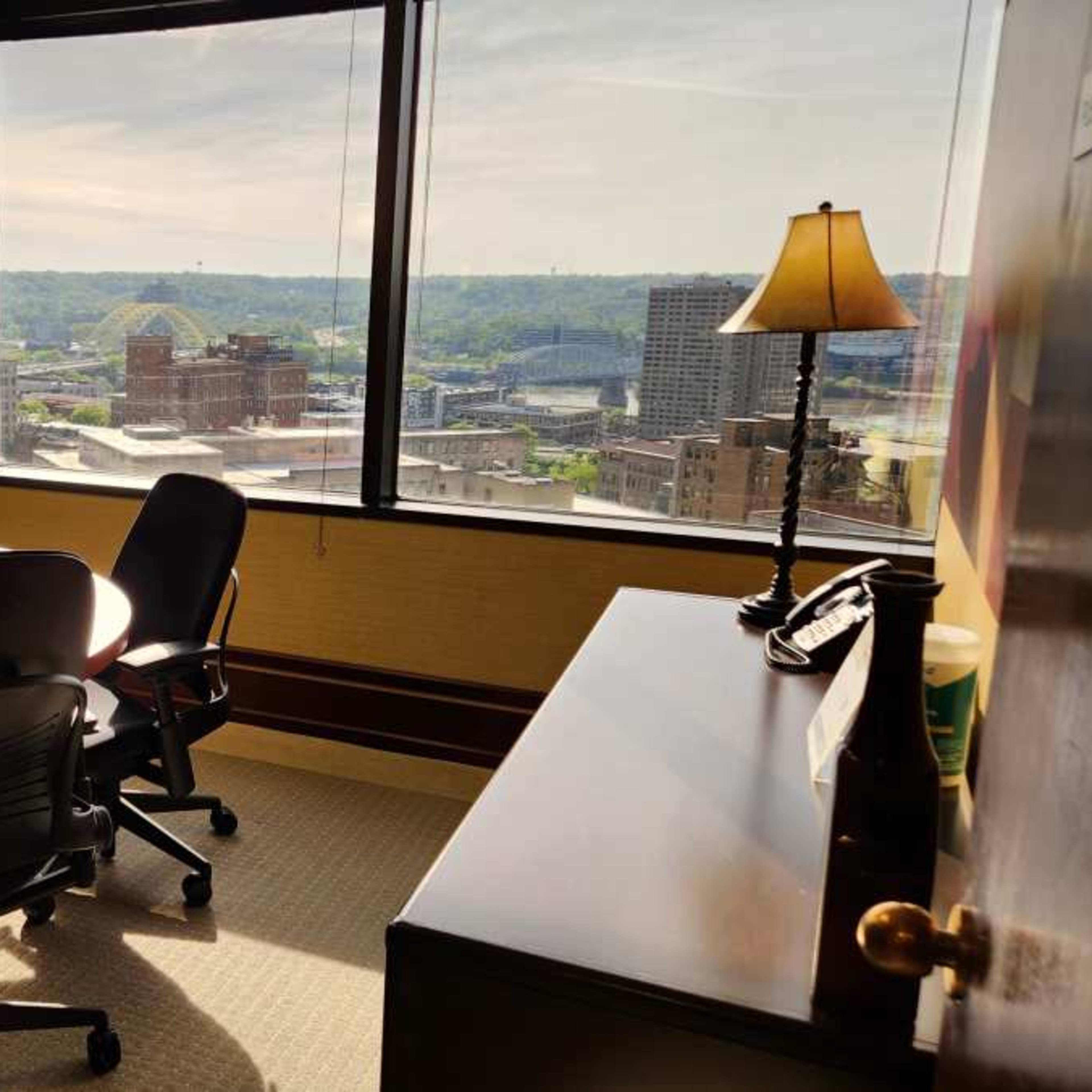 A conference room with a round table and four chairs offers a view of the city skyline through large windows.