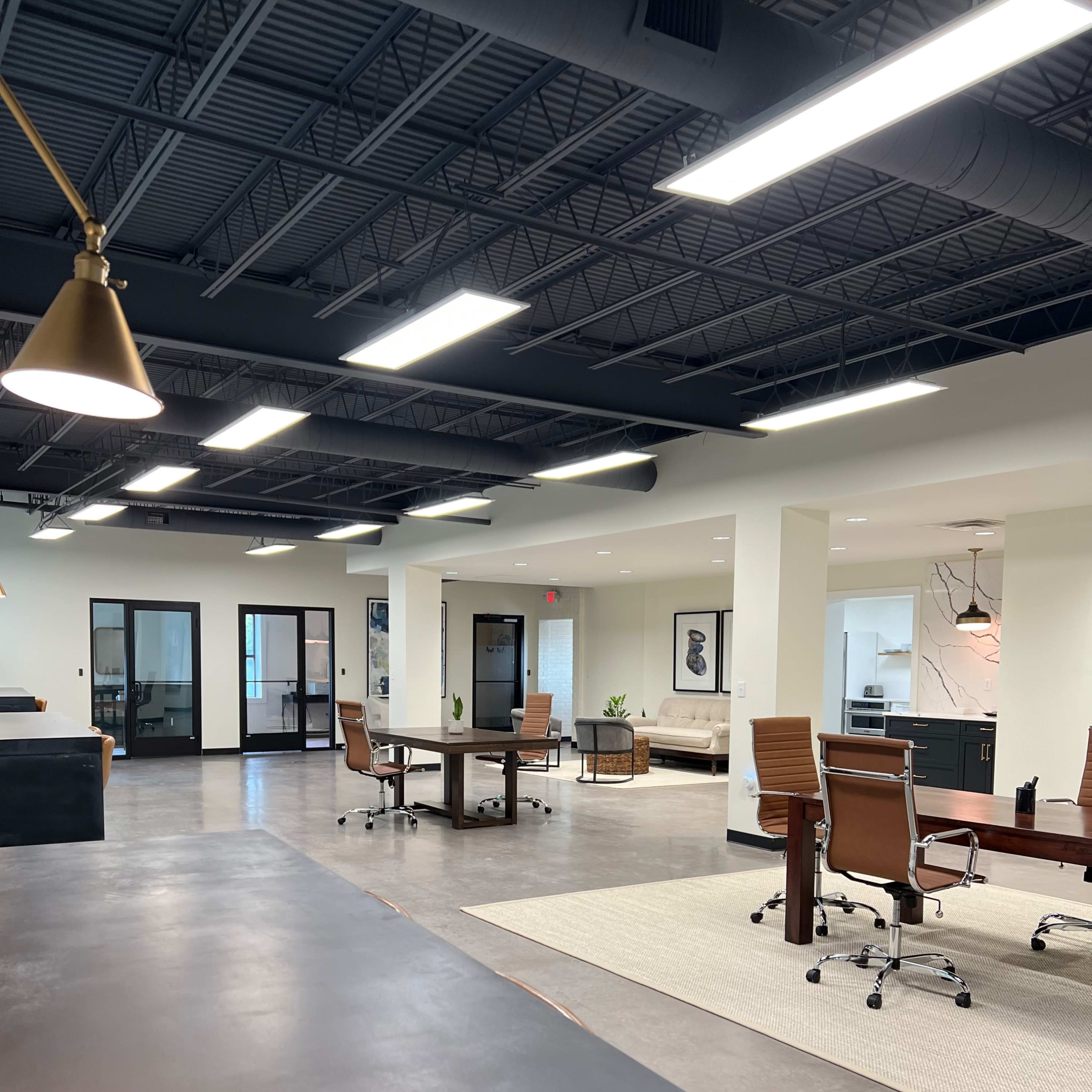A modern open office space featuring several workstations, a conference area, and natural light streaming through large windows.