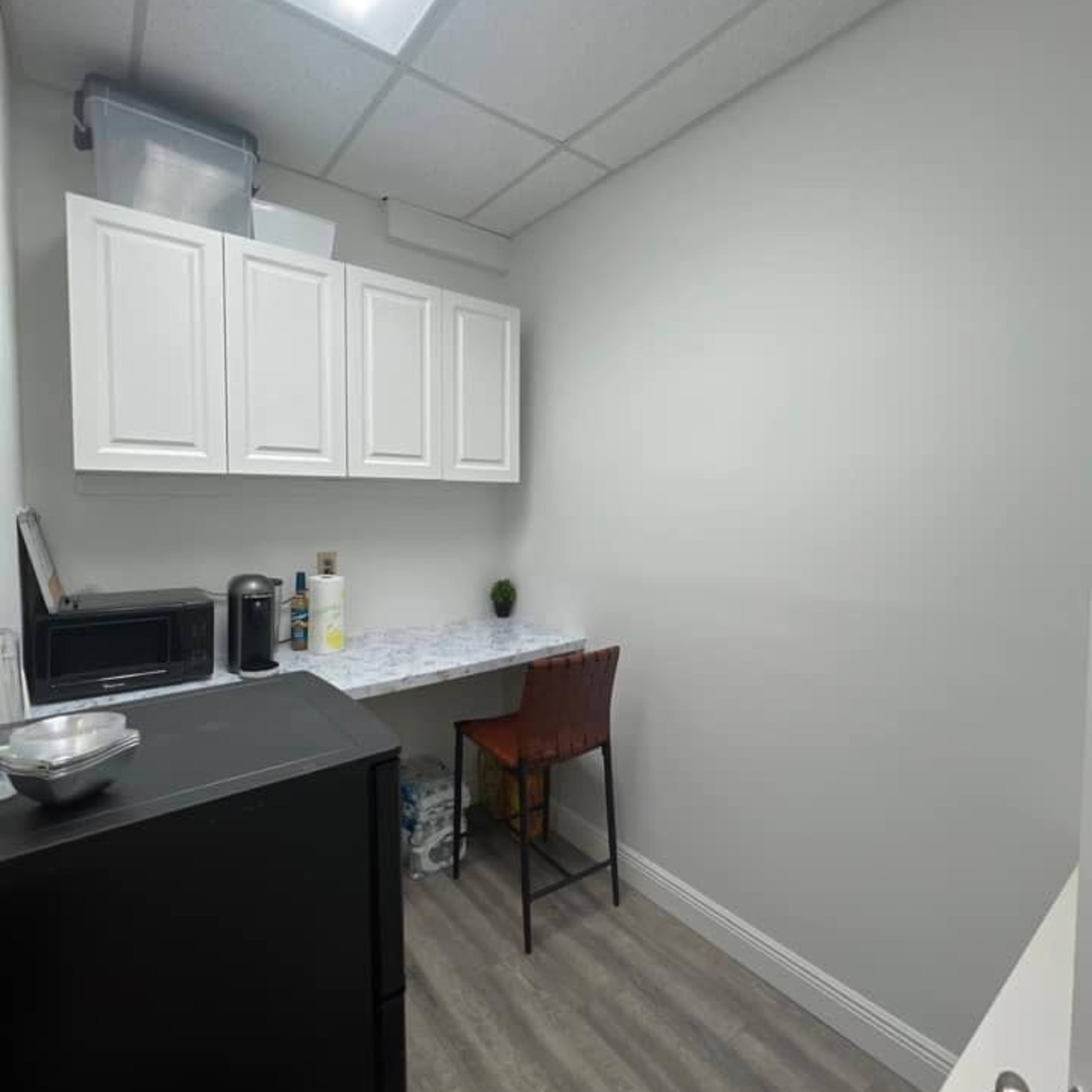 A small kitchen area with a black refrigerator, a microwave, white cabinets, and a wooden chair beside a countertop.