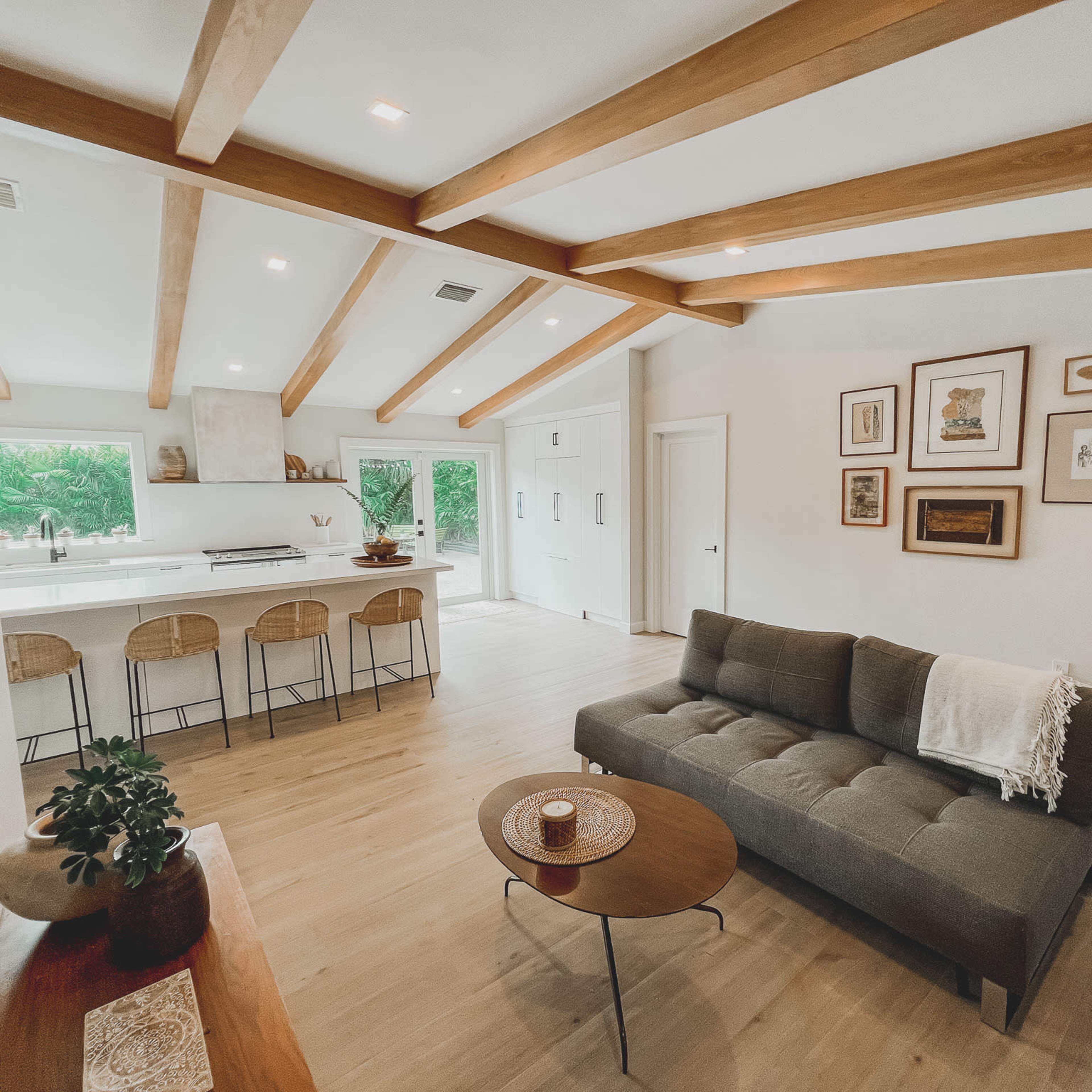 A modern living room with a sectional sofa, wooden beam ceilings, and an open kitchen area in the background.