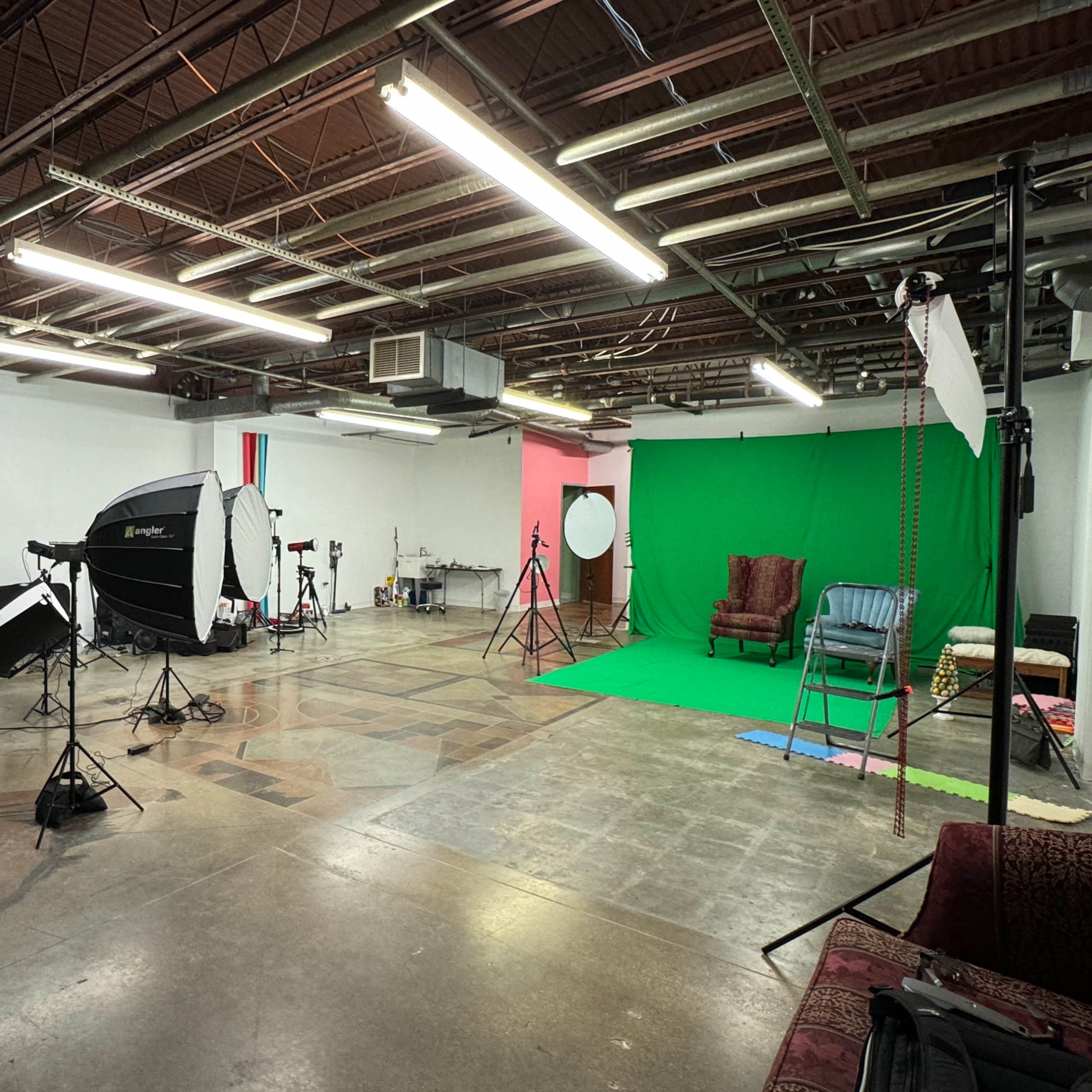 A photography studio with a green backdrop, lighting equipment, and various props scattered around.