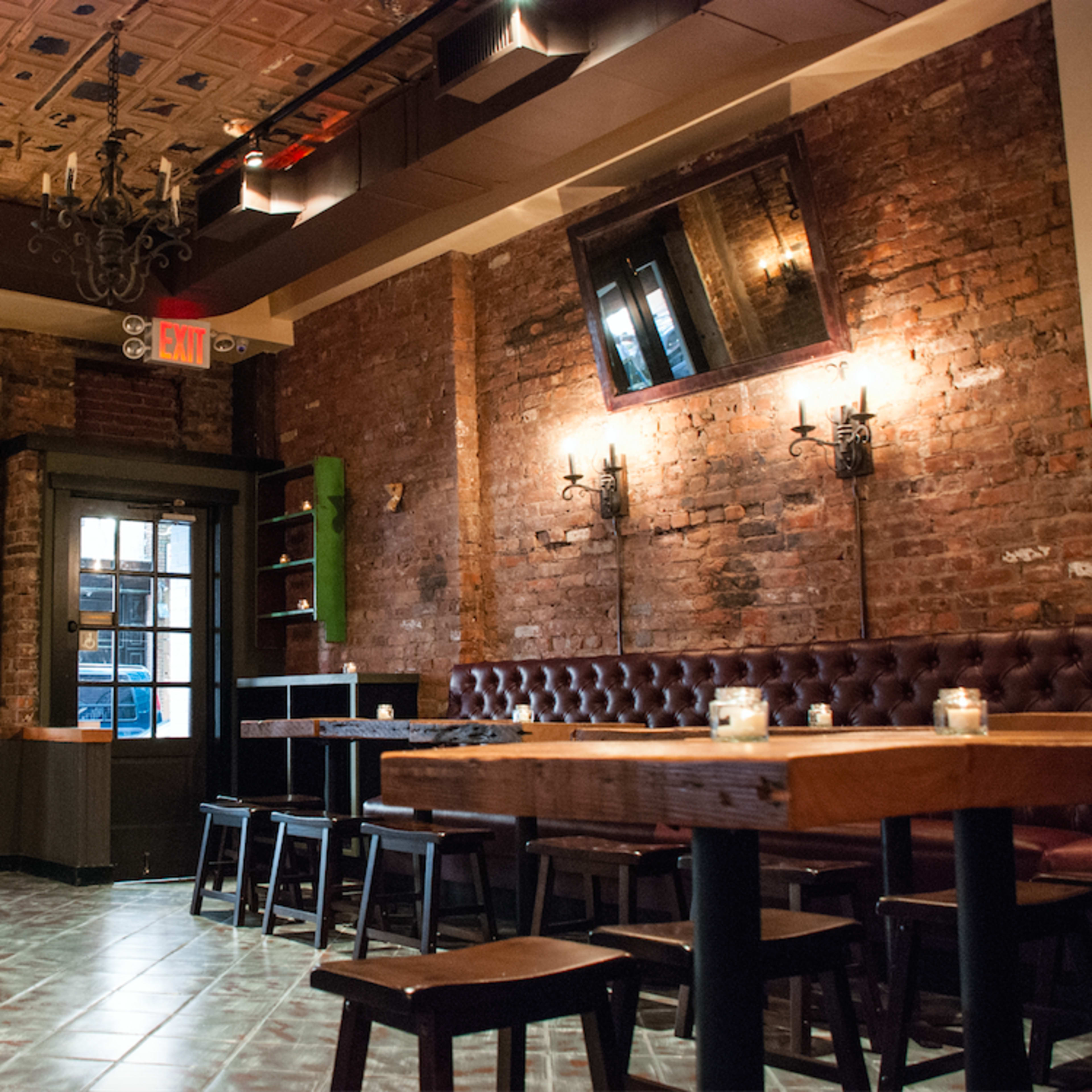 The interior of a restaurant featuring exposed brick walls, wooden tables, and a chandelier.