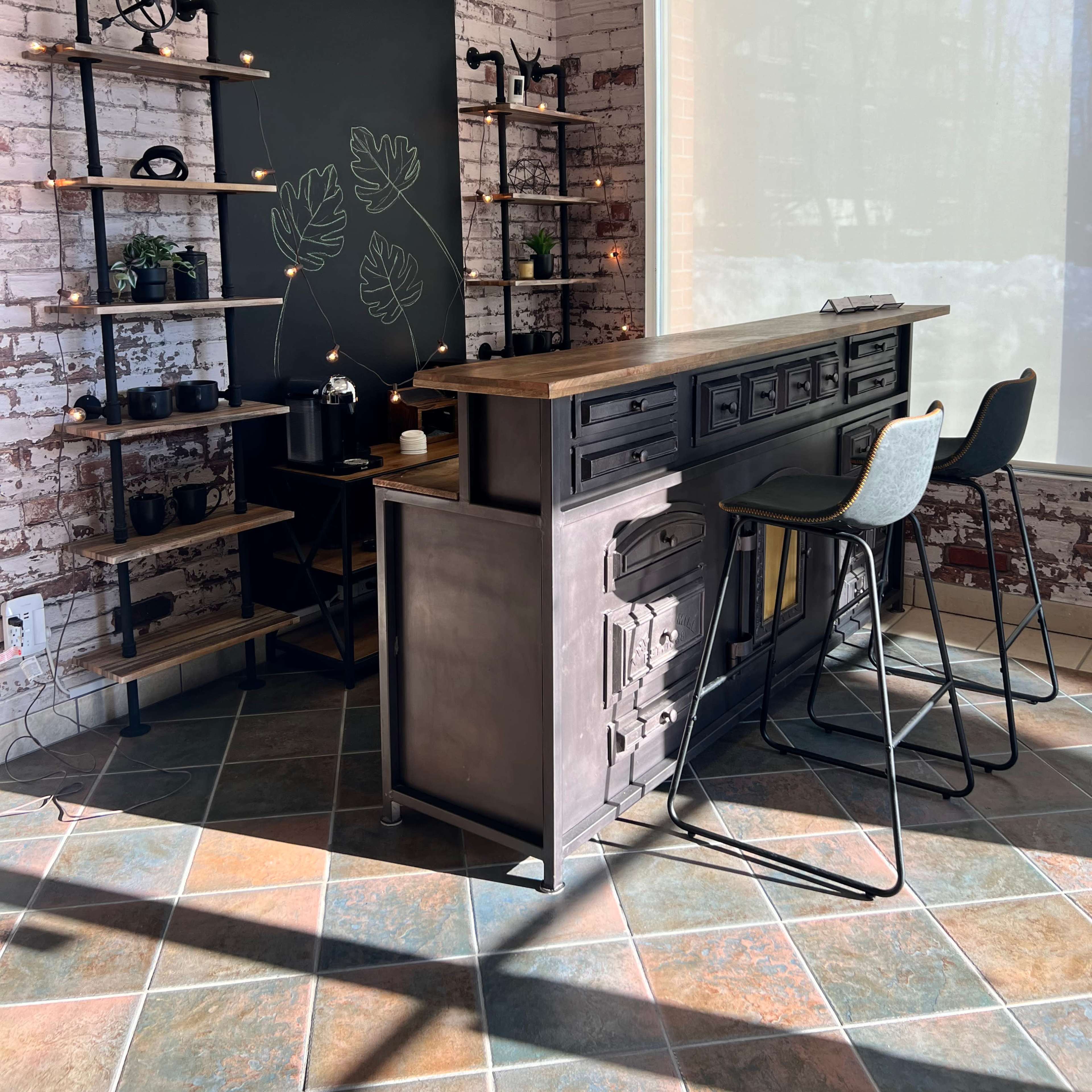 A modern café interior with a wooden bar, tall stools, and shelves displaying various items against a brick wall.