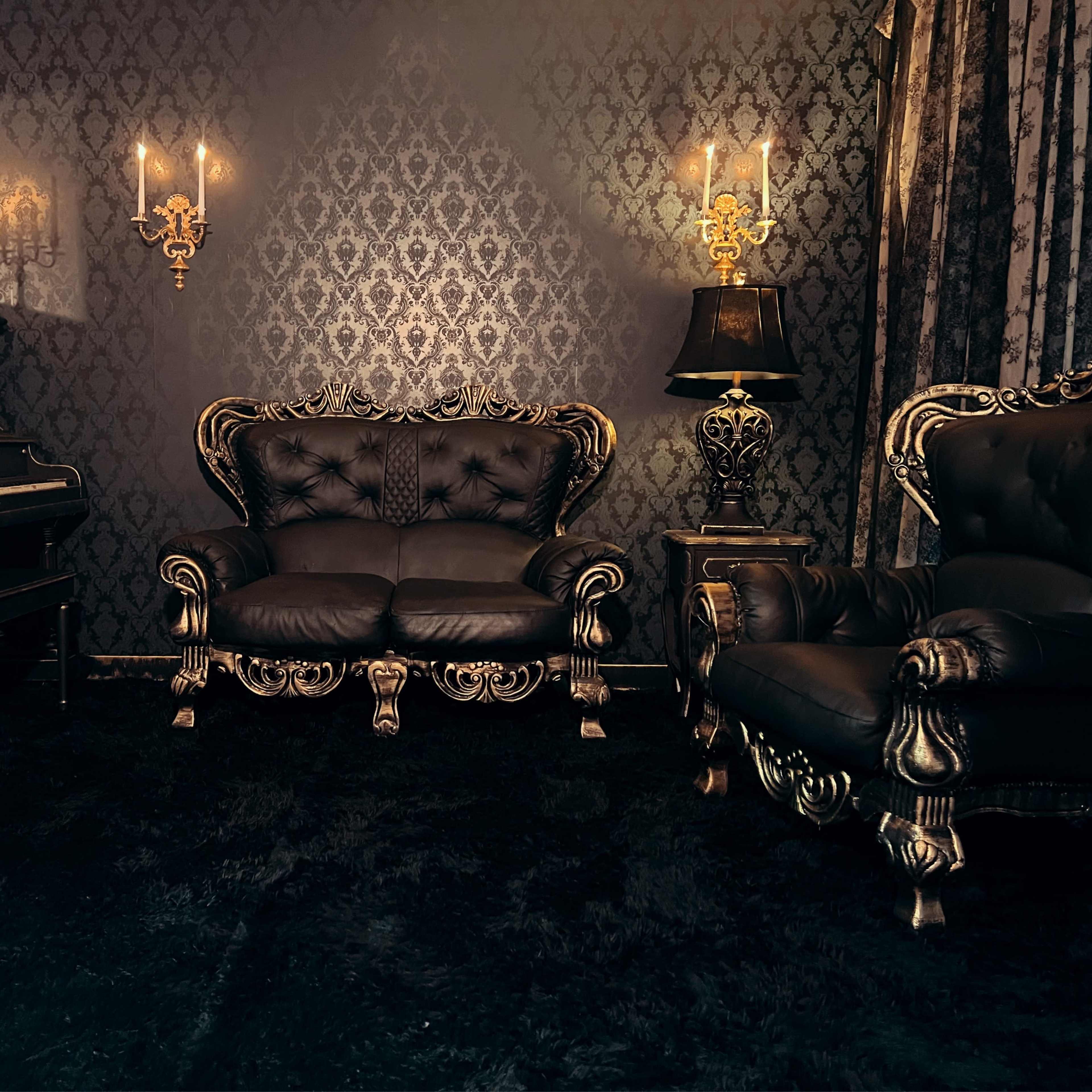 A darkly themed room with ornate furniture, including a black piano and a seating arrangement featuring a sofa and armchair, all adorned with golden accents against patterned wallpaper.
