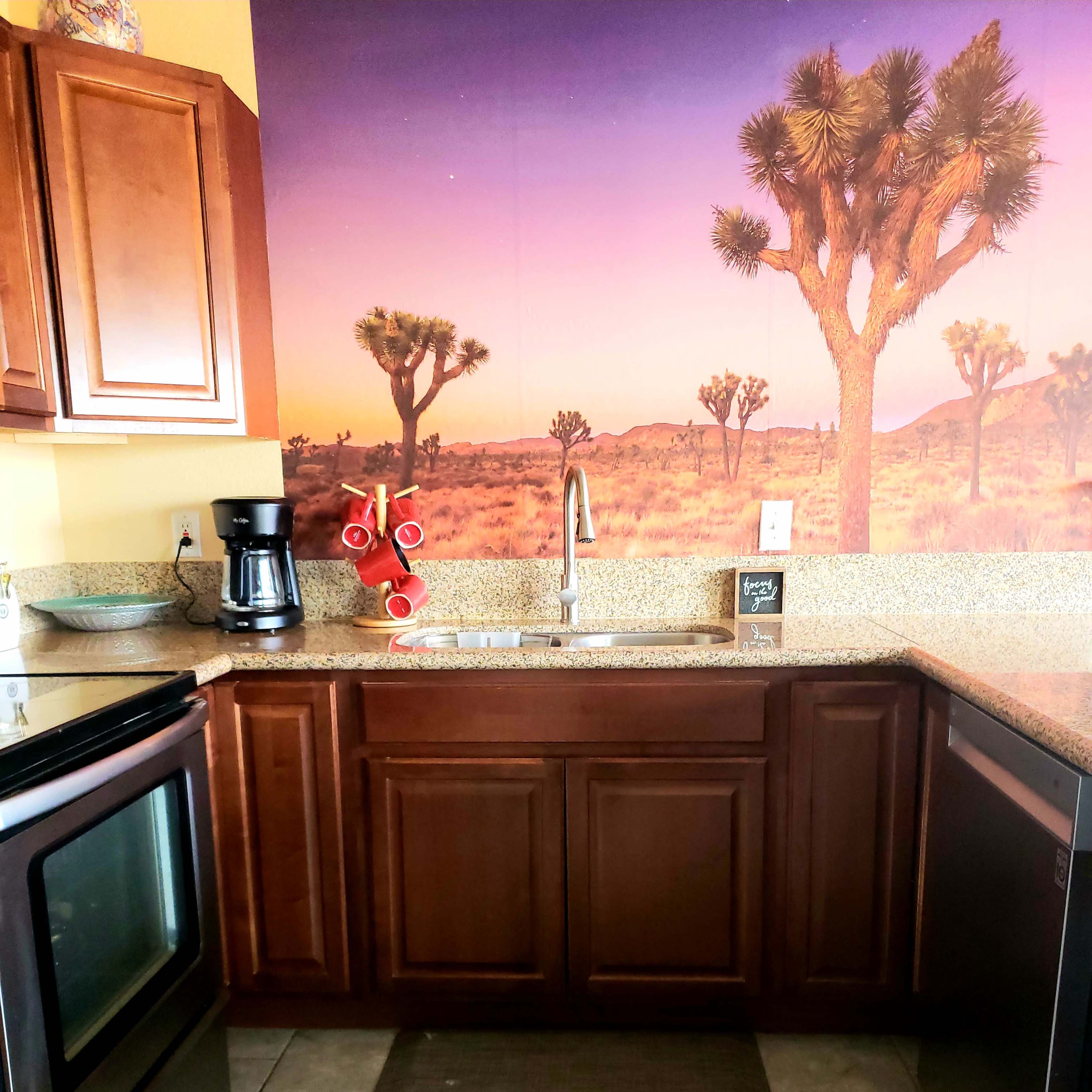 A kitchen with wooden cabinets, a granite countertop, a sink, and a wall featuring a desert landscape mural with Joshua trees.