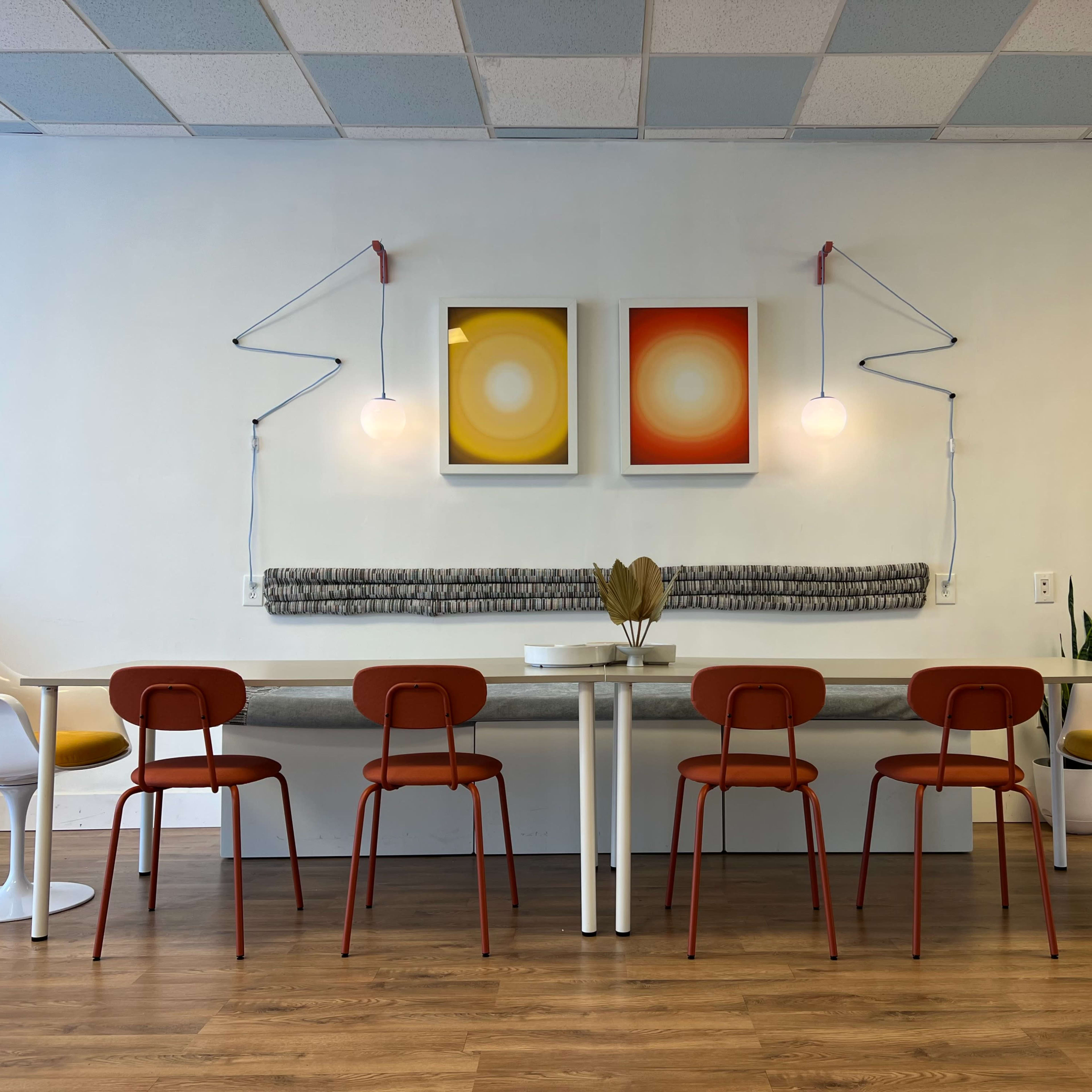 A modern dining area with a long table and six chairs, complemented by two framed circular artworks and pendant lights on the wall.