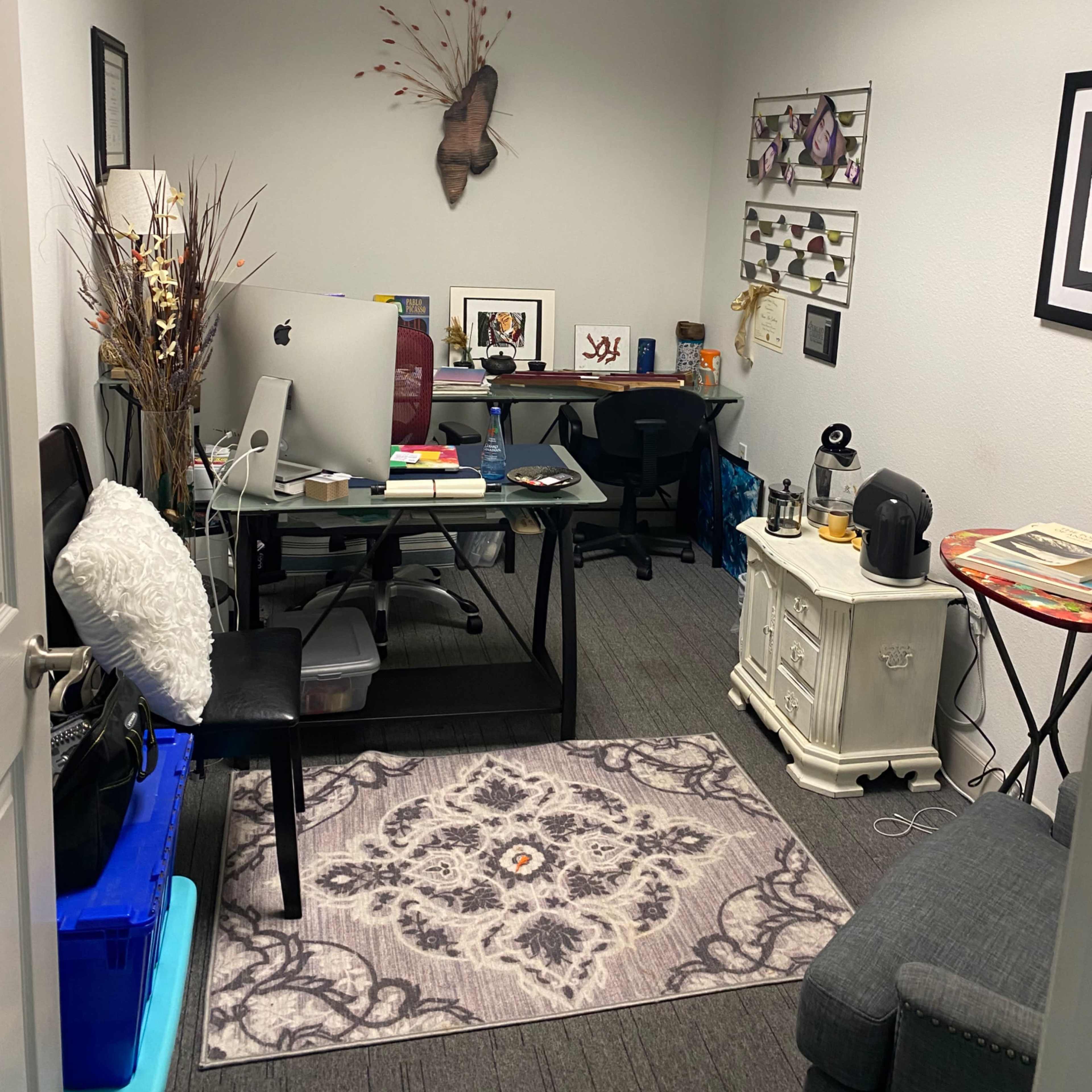 A small office space furnished with a desk, a computer, a chair, and decorative items on the walls.