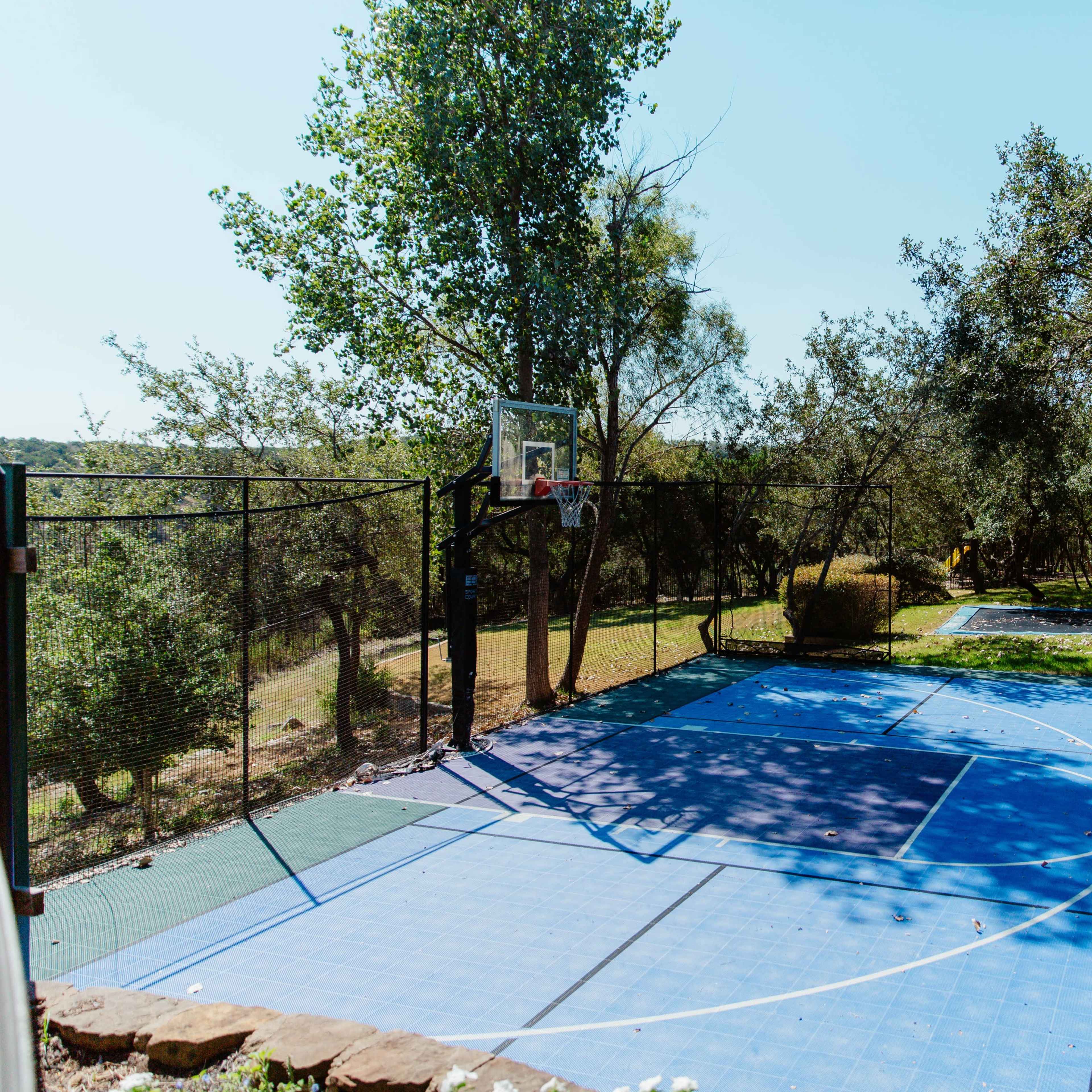 A basketball court surrounded by trees and shrubs, with a nearby area likely designed for another activity.