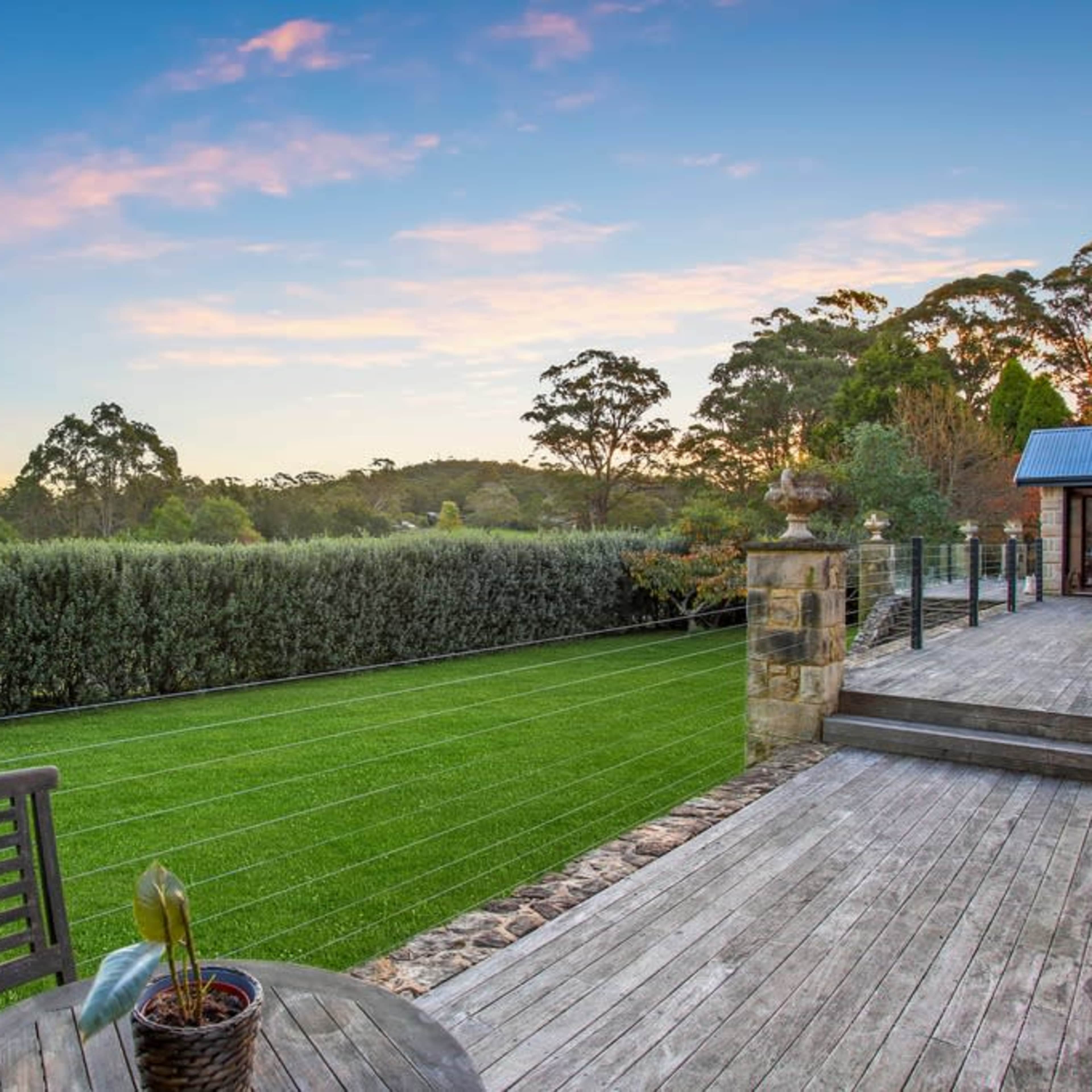 A wooden deck overlooking a green lawn bordered by trees under a colorful sky at sunset.